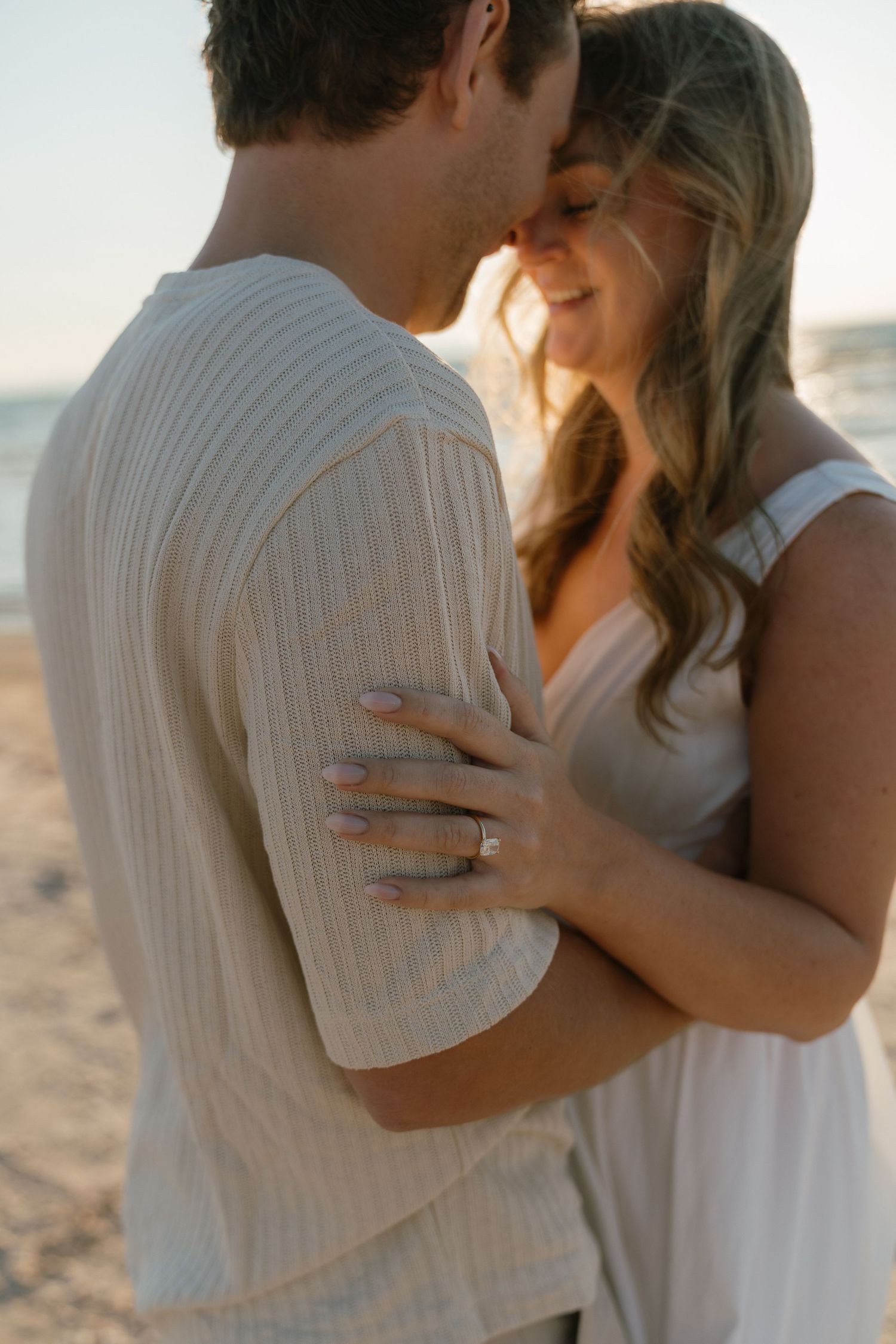 A romantic beach photoshoot featuring a couple in white clothing embracing.