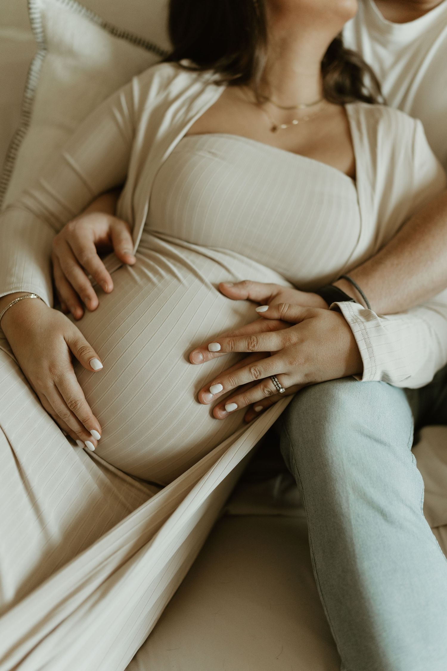 Gentle hands resting on a pregnant belly in soft, natural light.