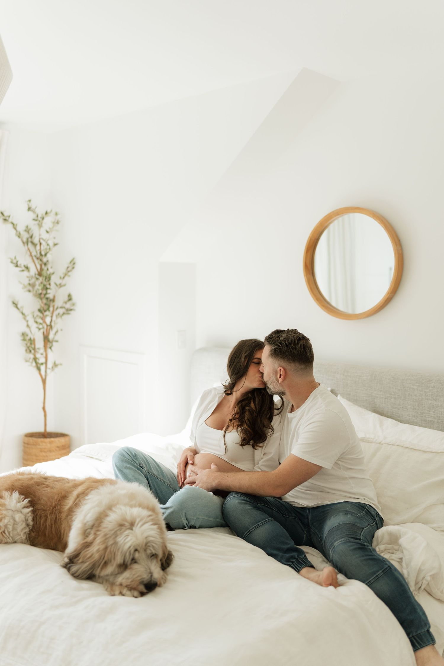 Couple relaxing on white bed with dog while sharing intimate moments.