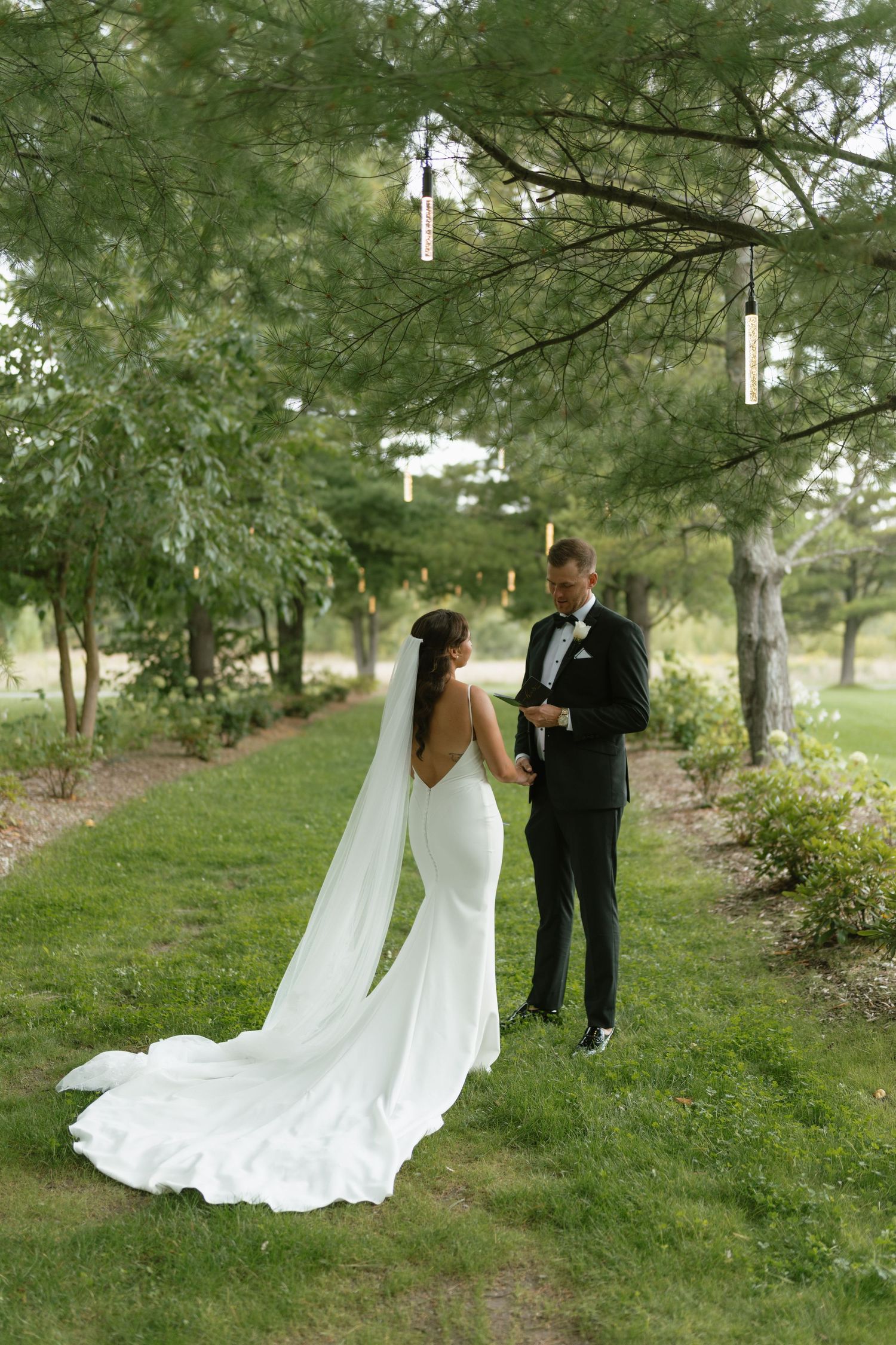 A flowing white wedding dress train trails behind on a green garden path.