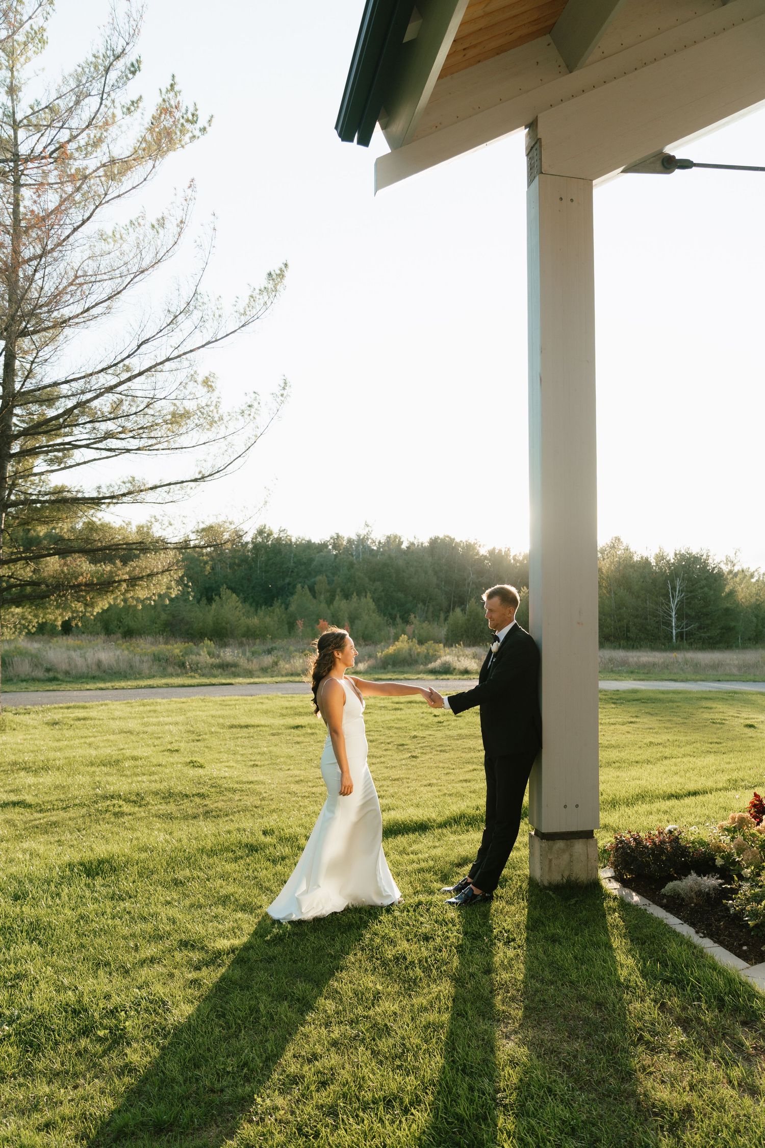 A couple shares a sunset moment under a white pillar on manicured grounds.