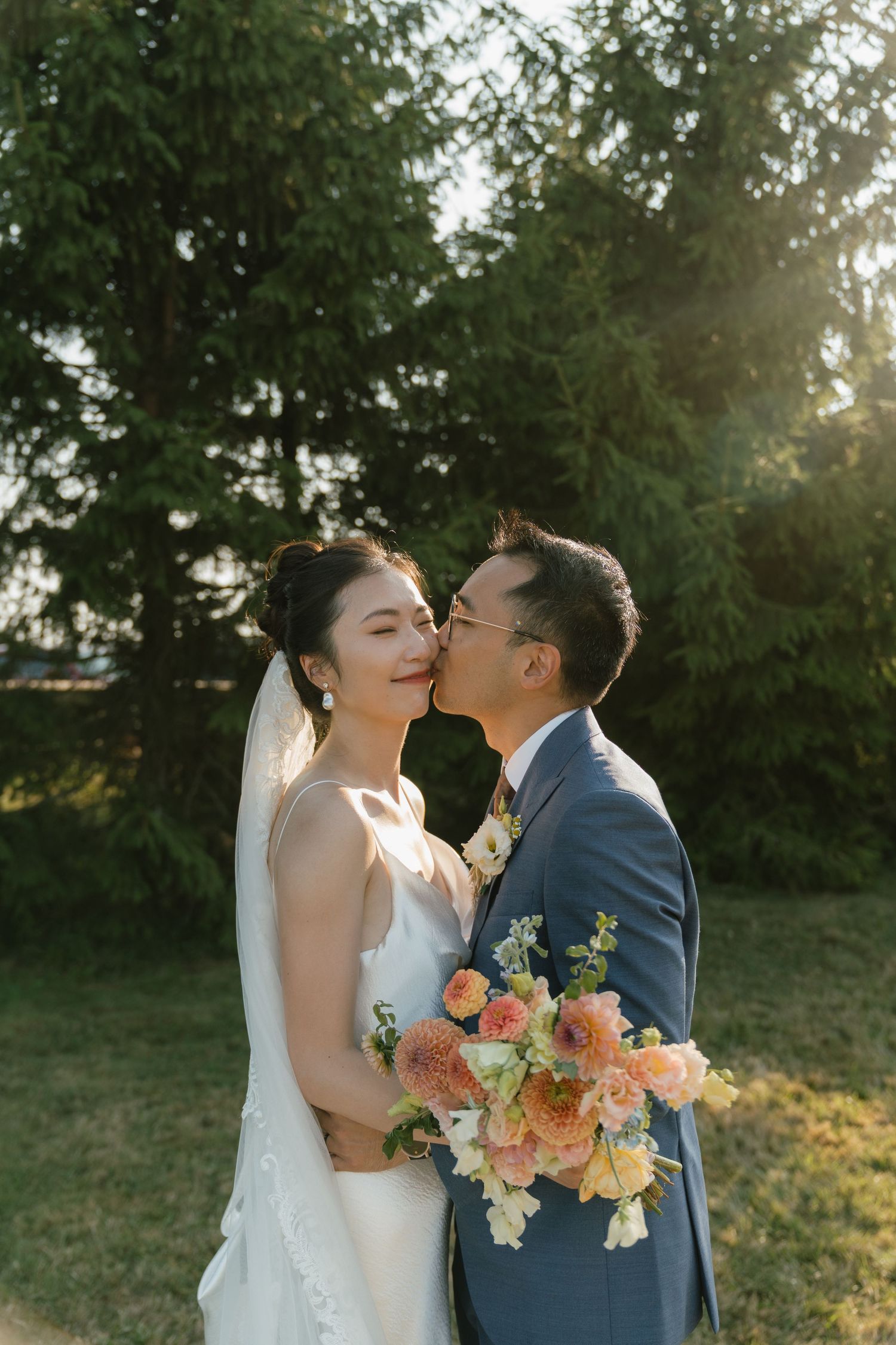 Wedding couple shares romantic kiss with colorful bouquet during sunset ceremony.