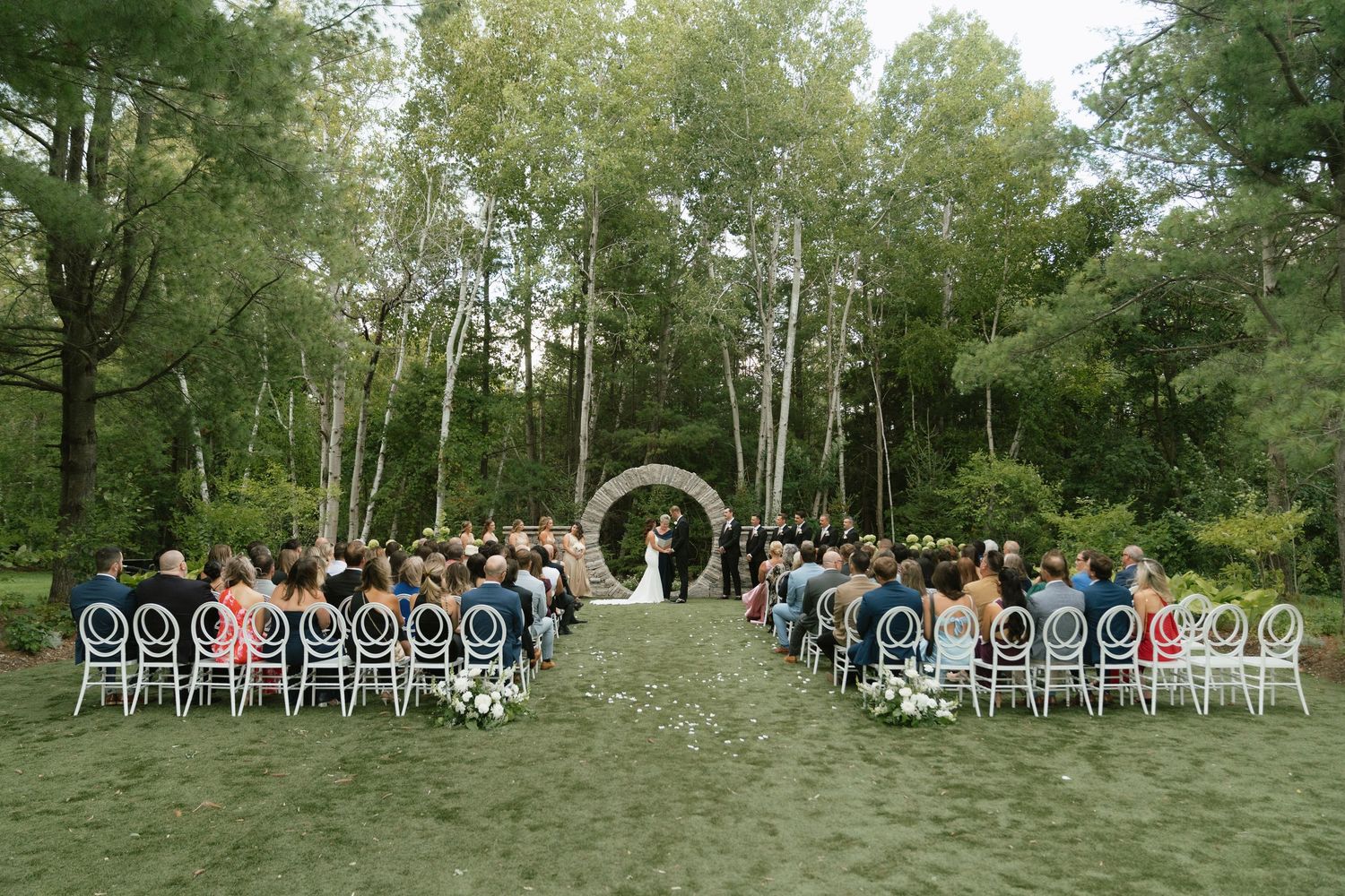 White chairs arranged in rows for an outdoor wedding ceremony in a wooded setting.