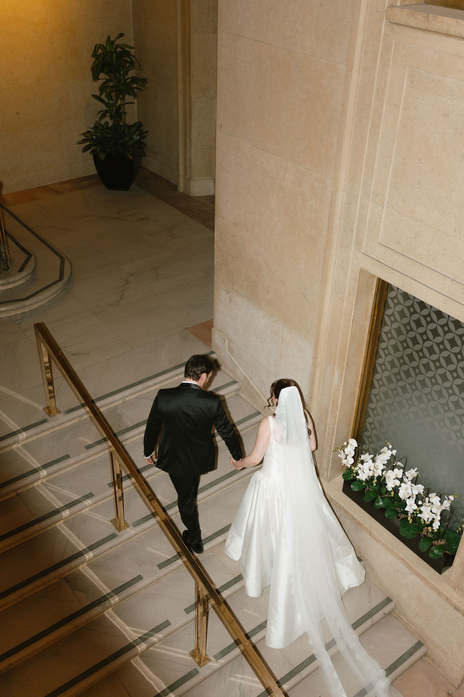 Couple descending marble staircase in formal wedding attire.