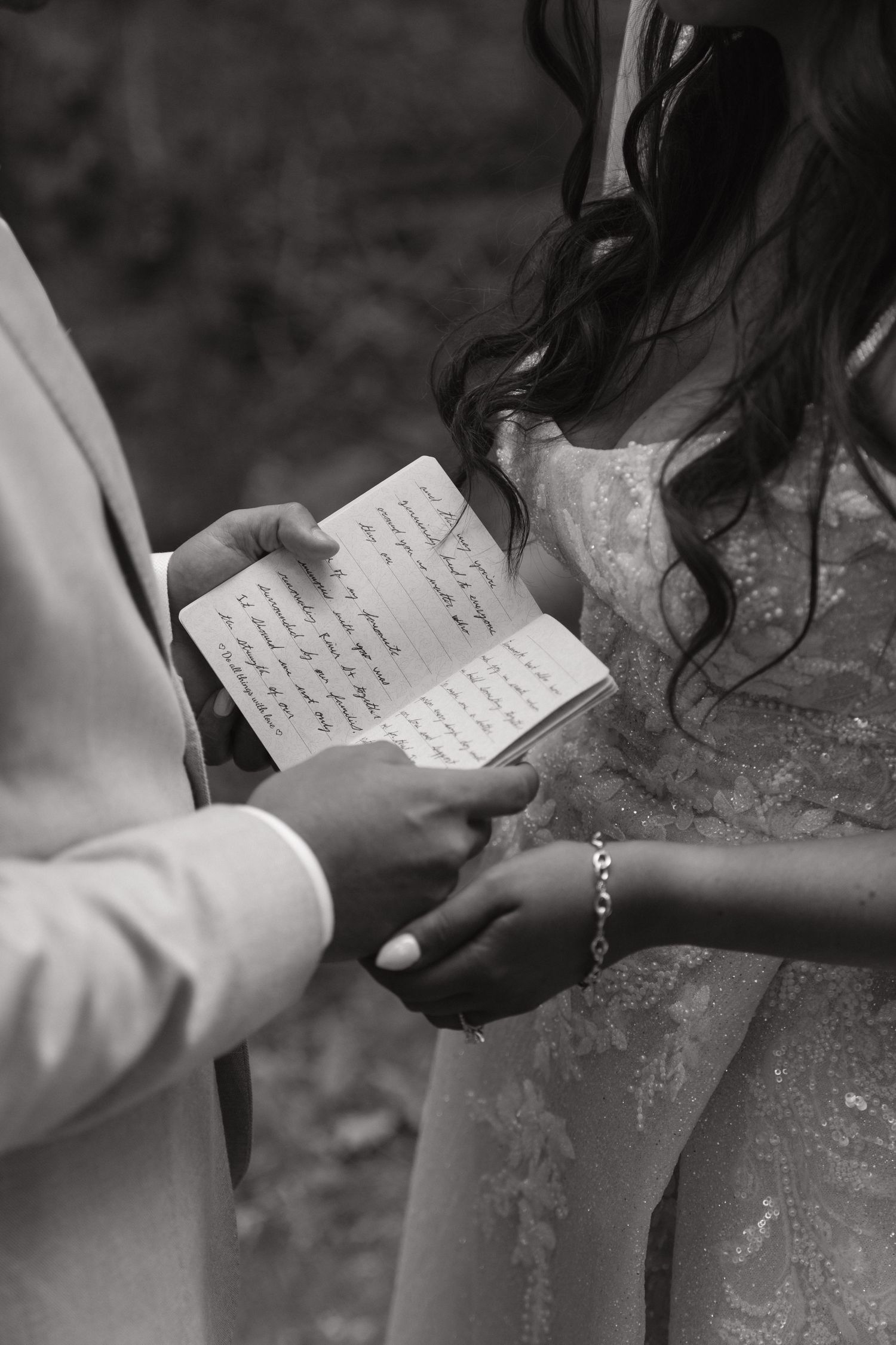 A black and white image of hands holding handwritten wedding vows during a ceremony.