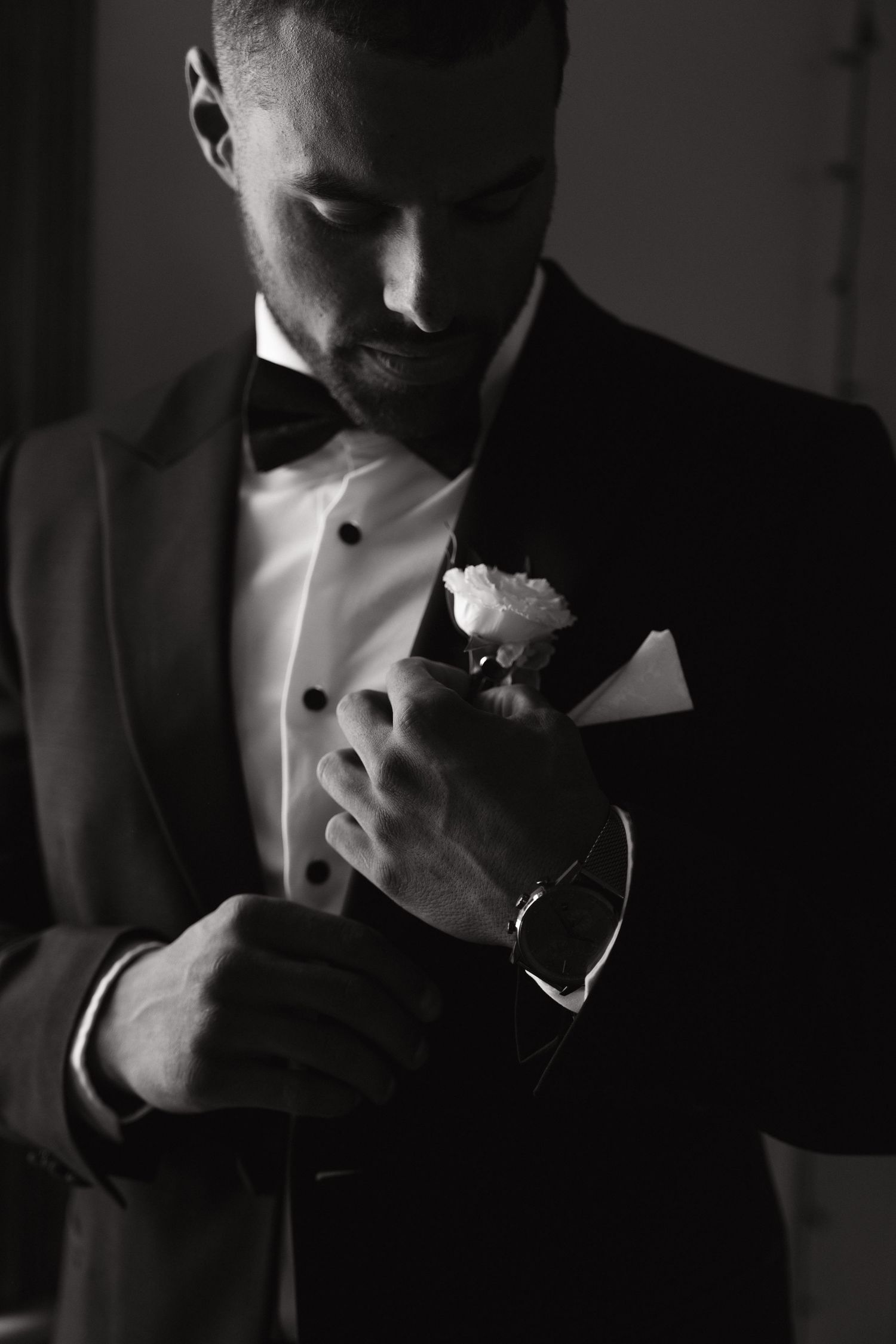 Dramatic black and white portrait of groom adjusting boutonniere.