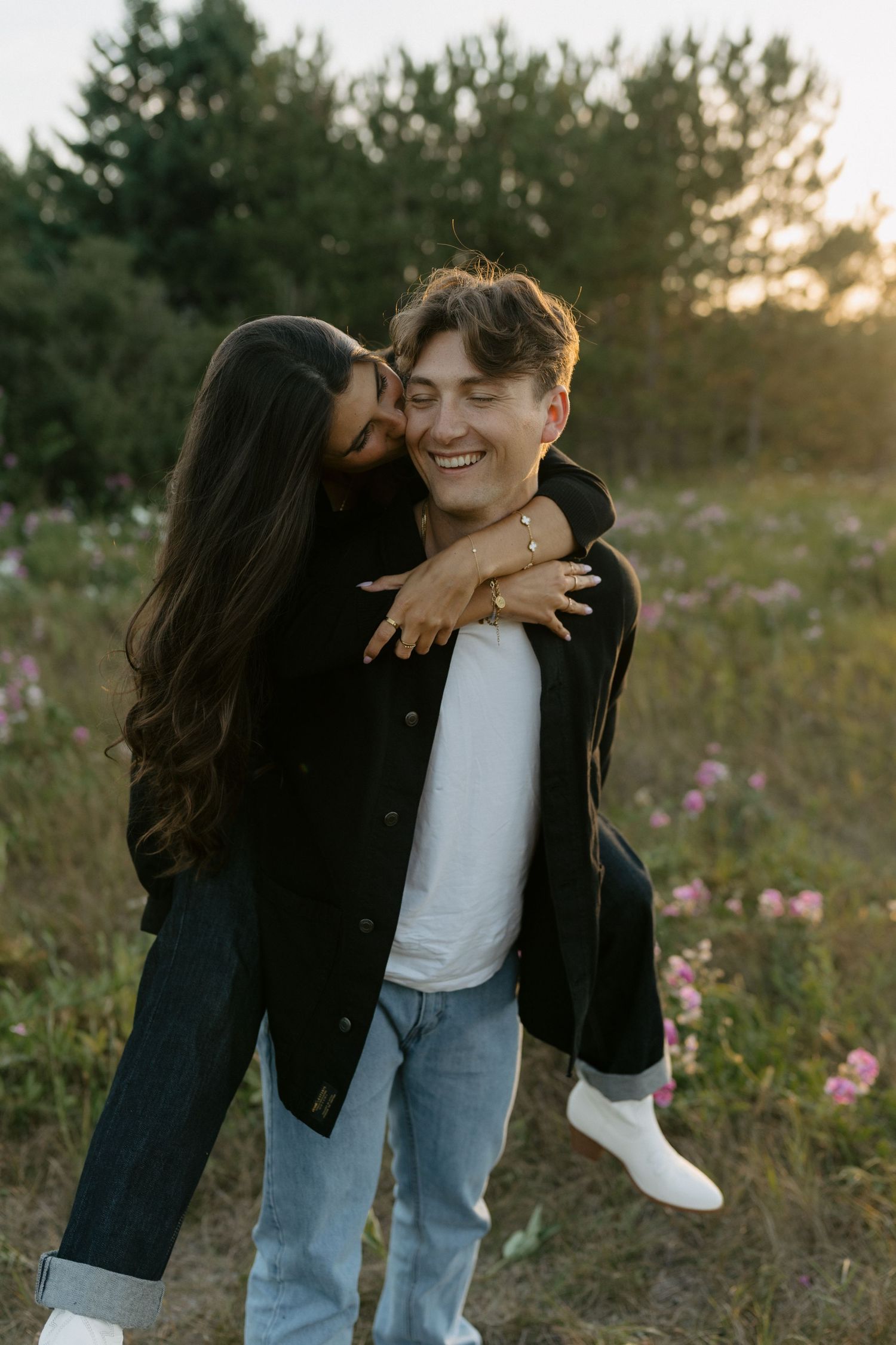 Playful couple embracing in field of wildflowers at golden hour.