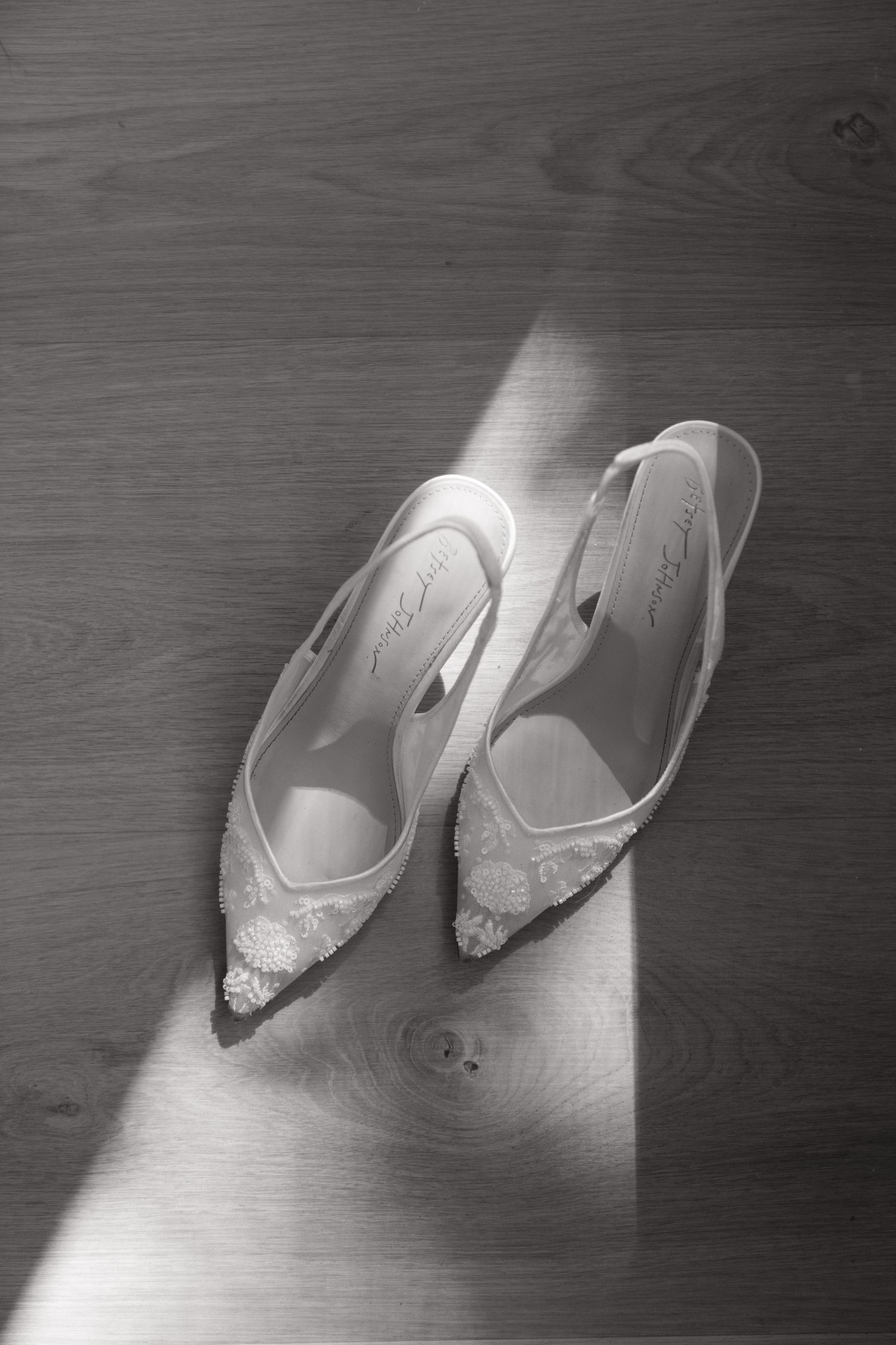 Elegant white lace bridal shoes on a wooden floor with dramatic lighting.