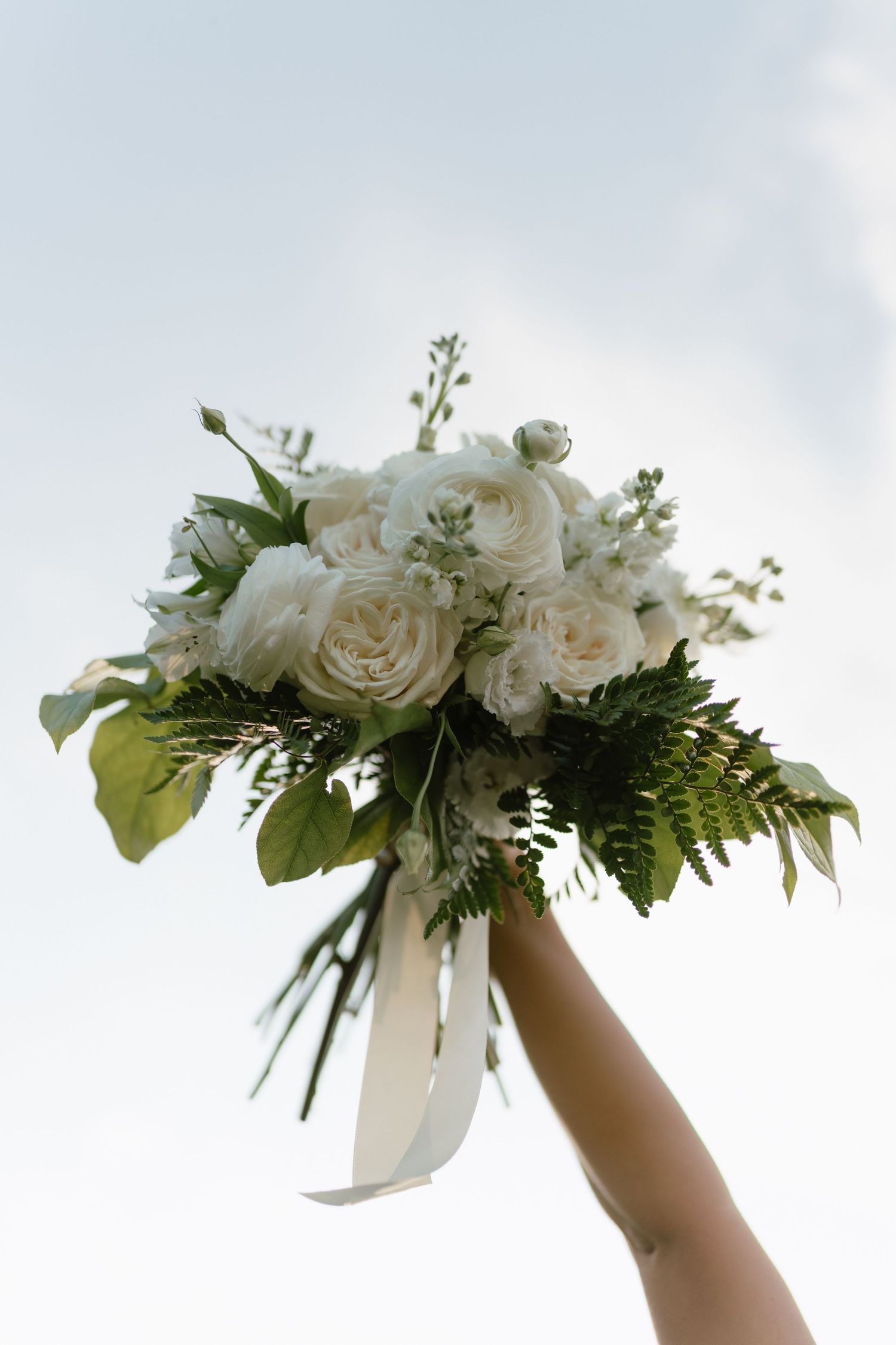 White roses and greenery form an elegant floral garland held up against a bright sky.