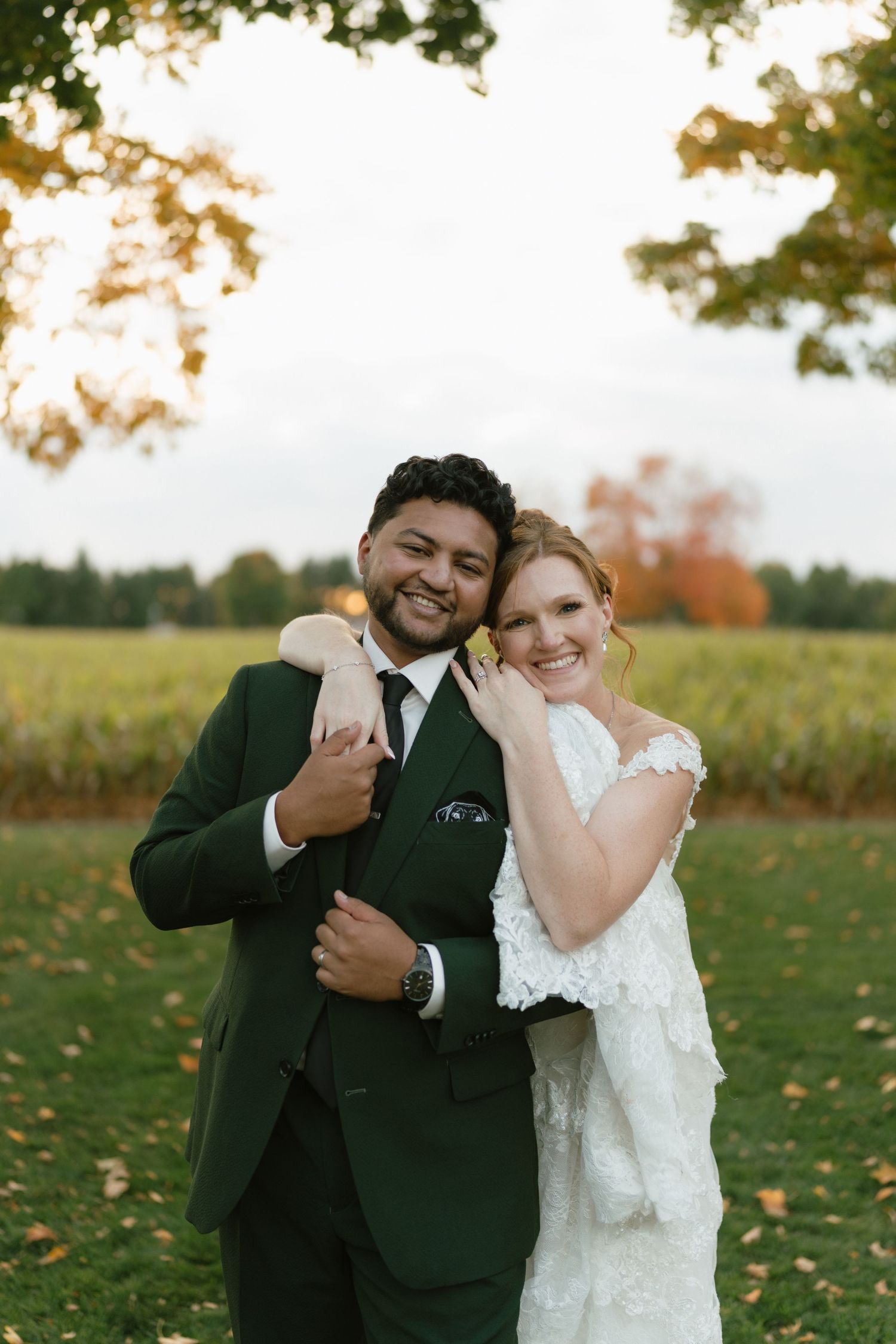 A joyful wedding couple poses together in an autumn field at sunset.