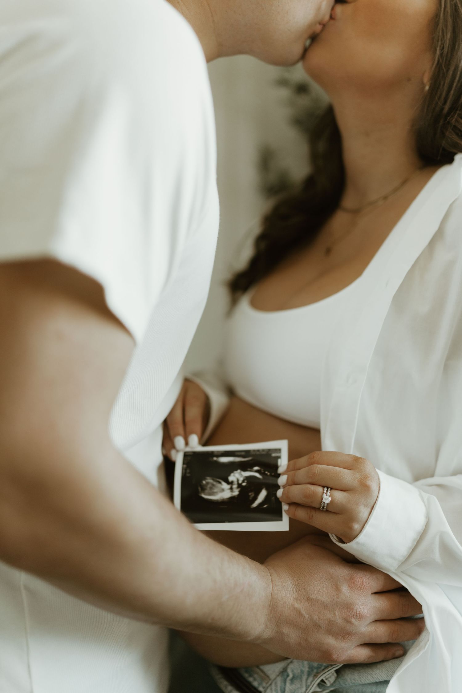Someone in white holding an ultrasound photo against their chest.