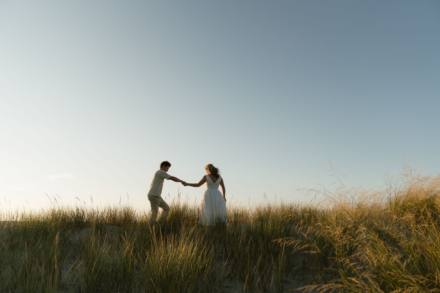 Silhouetted couple holding hands on grassy hilltop during sunset.