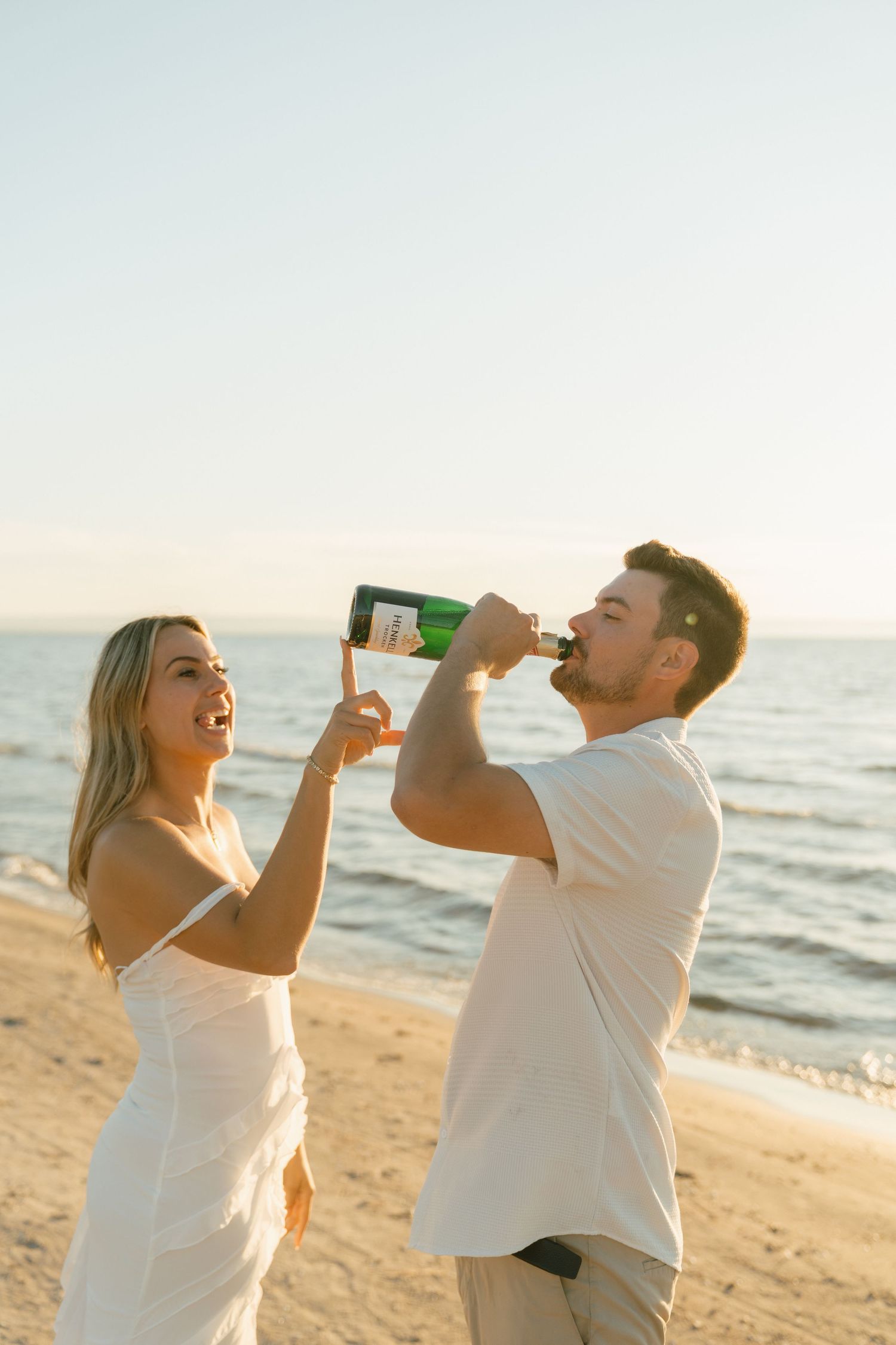Playful couple drinking beverages together on beach at sunset.
