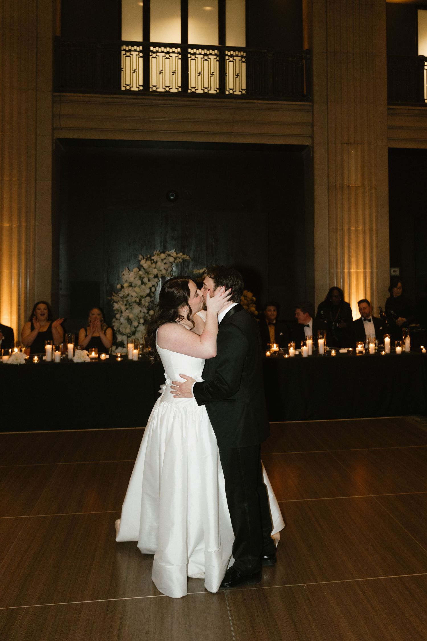 Romantic first dance in elegant ballroom with candlelit backdrop.