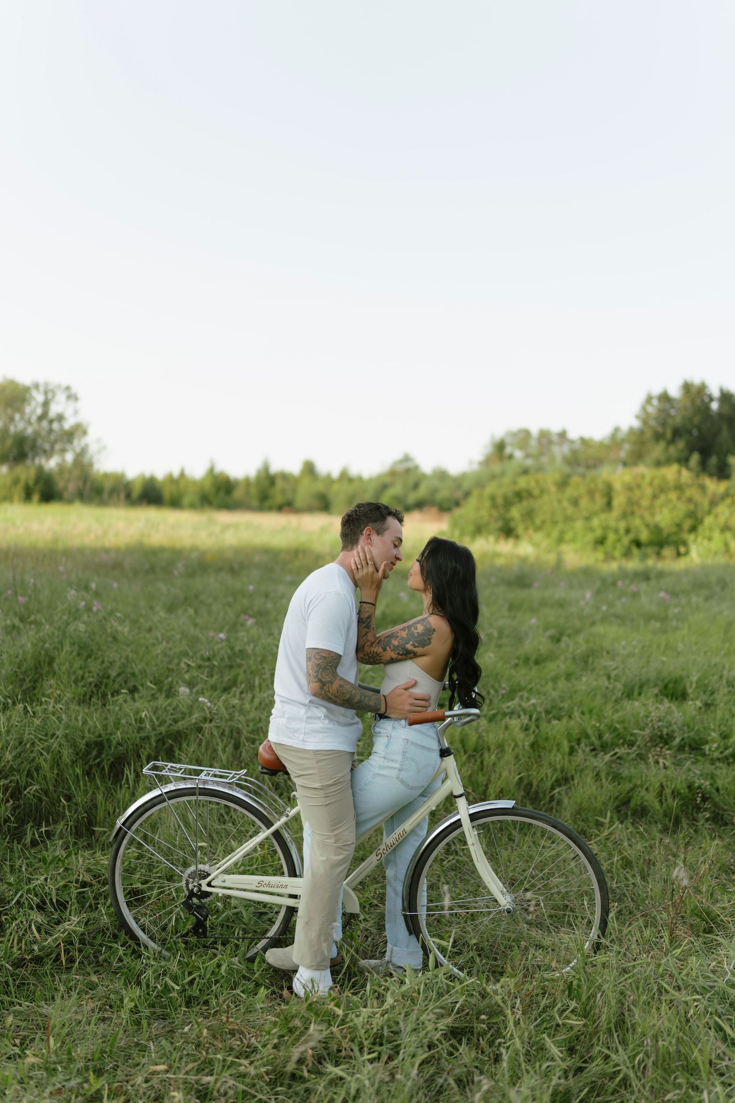 Couple sharing a romantic moment beside a vintage bicycle in a lush green field on a sunny day.
