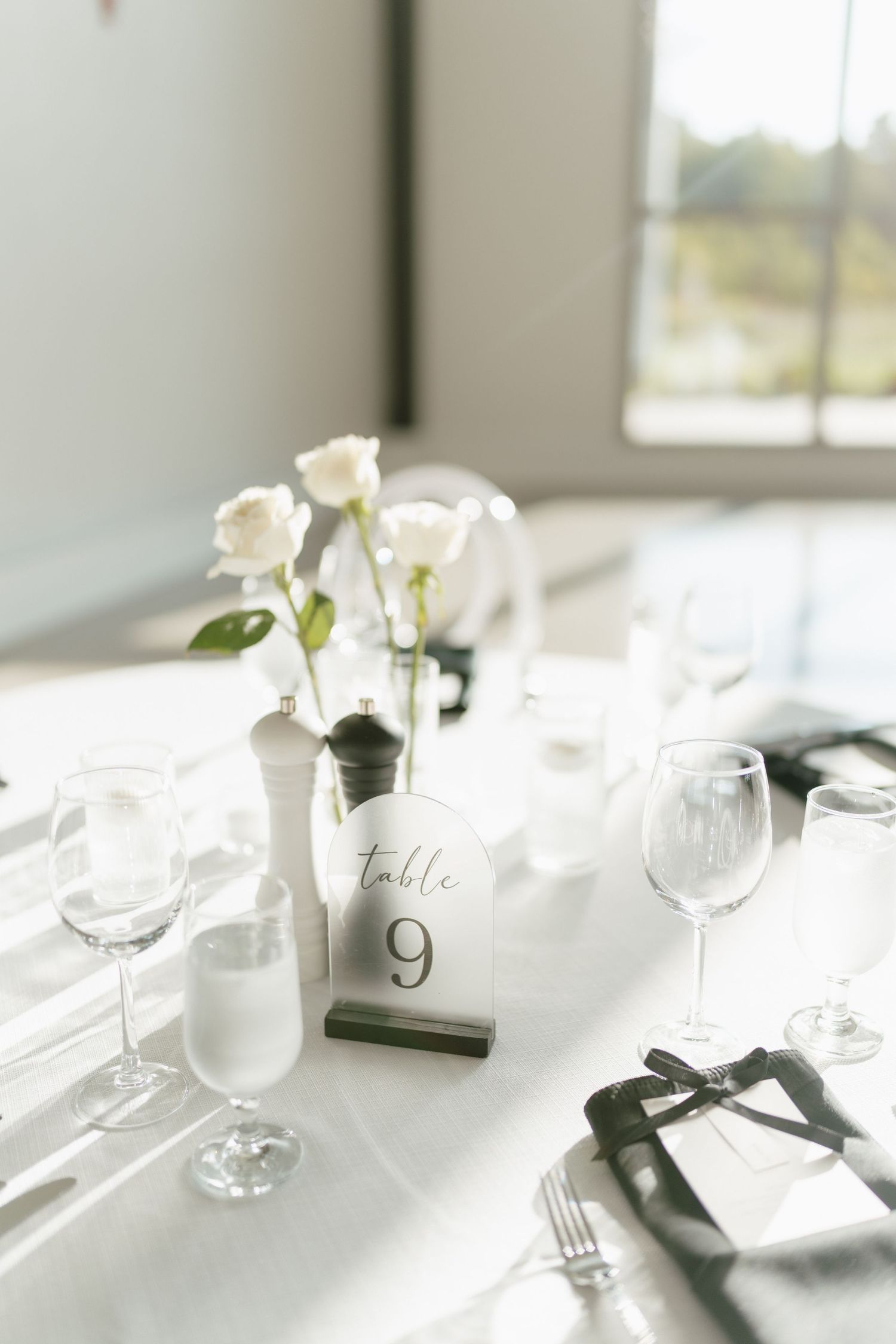 Elegant wedding table setting with white roses, wine glasses and table number 9.