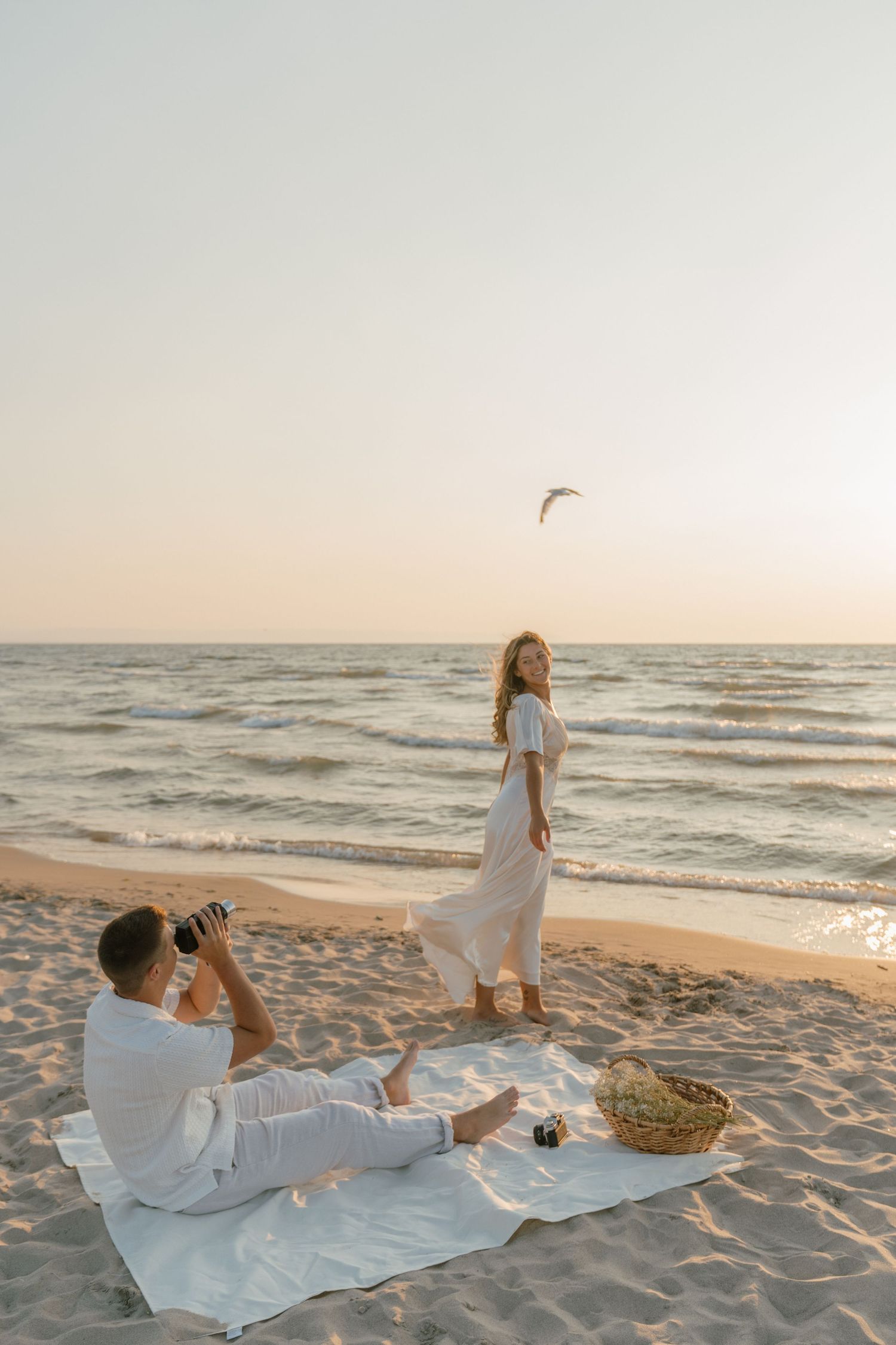 Couple having romantic beach picnic at sunset while taking photos.