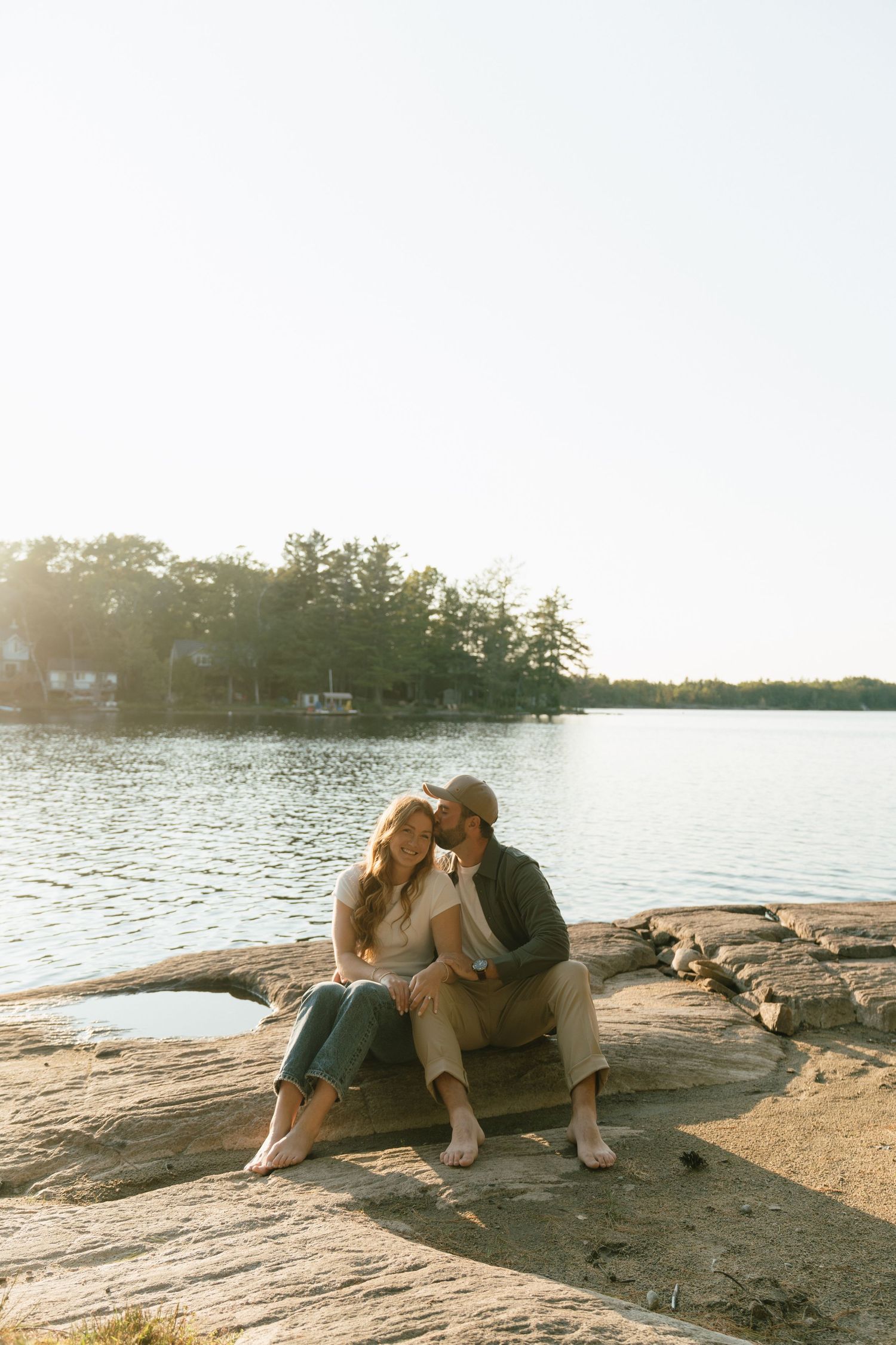 Couple sharing intimate moment on rocky shore at sunset with dog nearby.