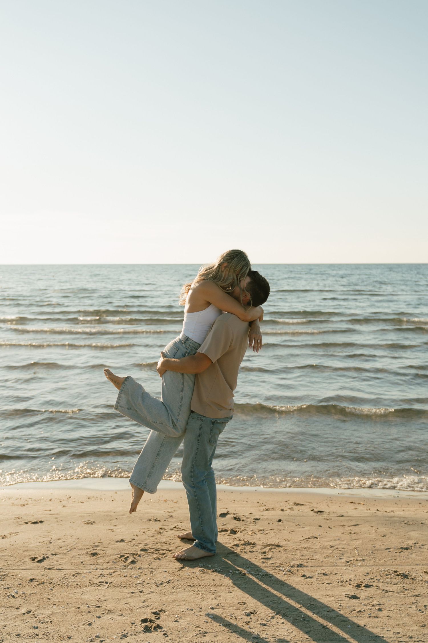 A couple dances and spins together on a sunny beach by the ocean.