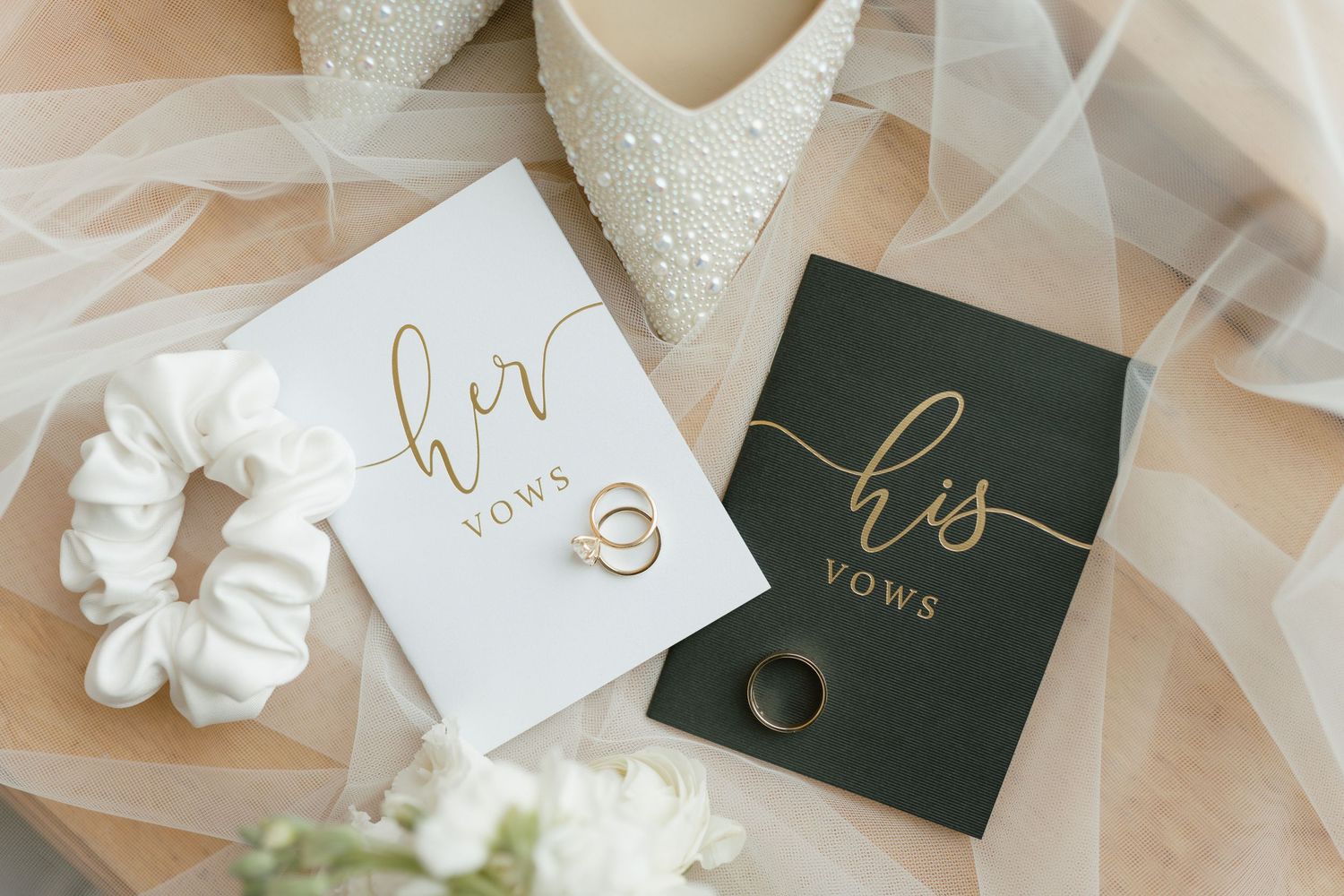 His and hers vow books with gold lettering displayed with wedding rings.