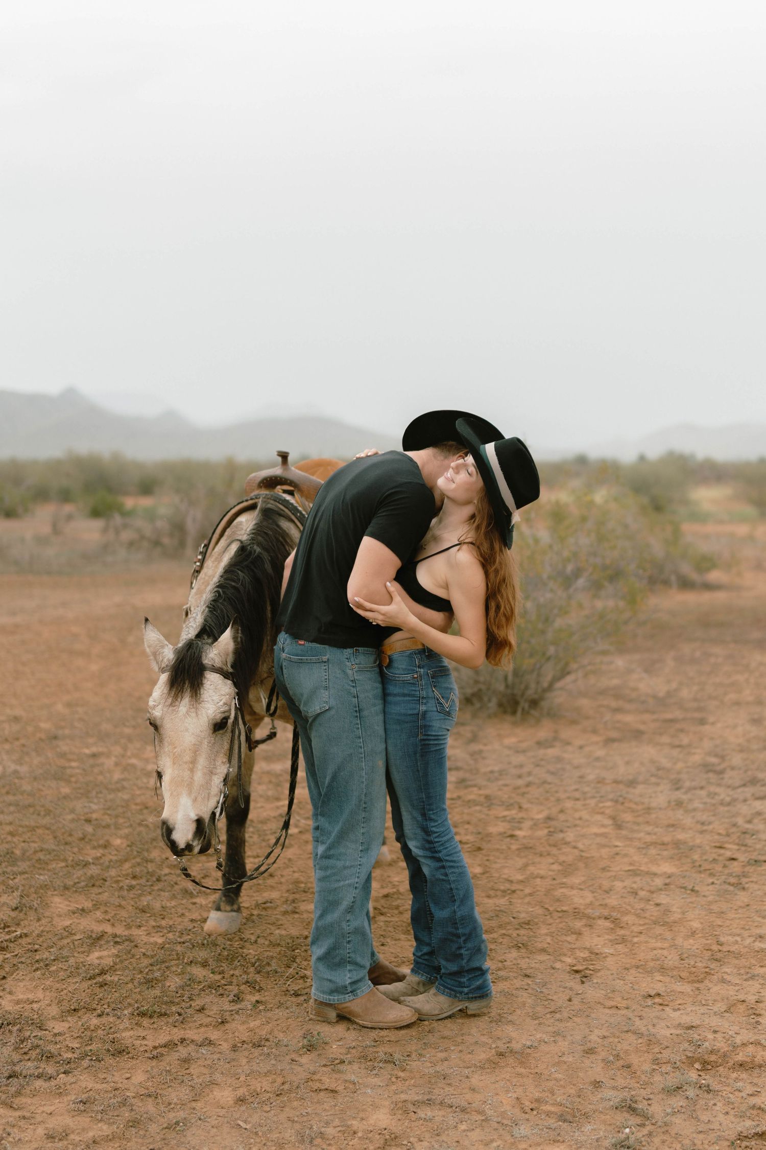 Romantic western scene with couple embracing beside horse in desert landscape.