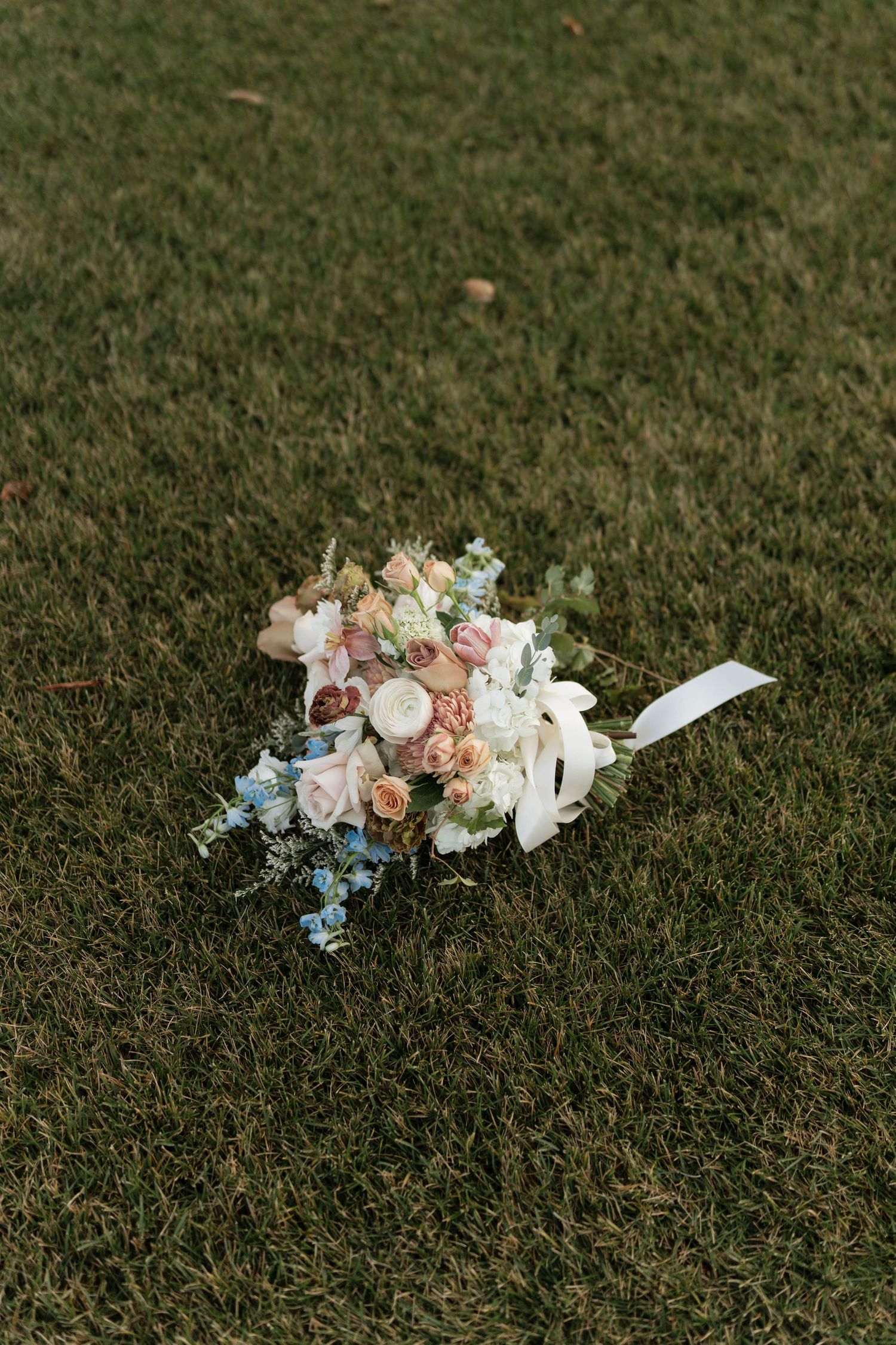 Delicate bridal bouquet with pink and white flowers lying on green grass.