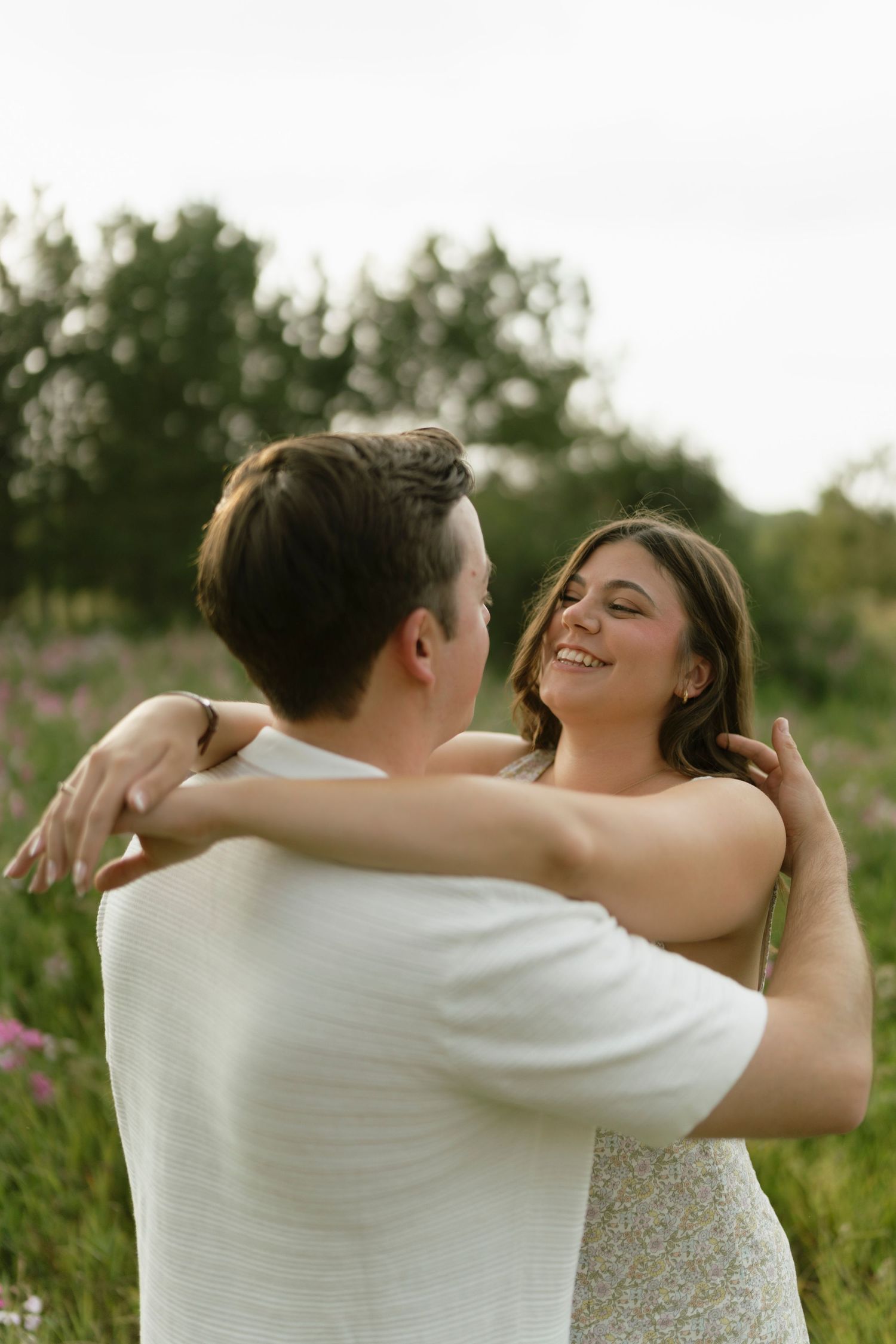 A smiling couple dancing together in a lush green field with wildflowers, sharing a joyful romantic moment.