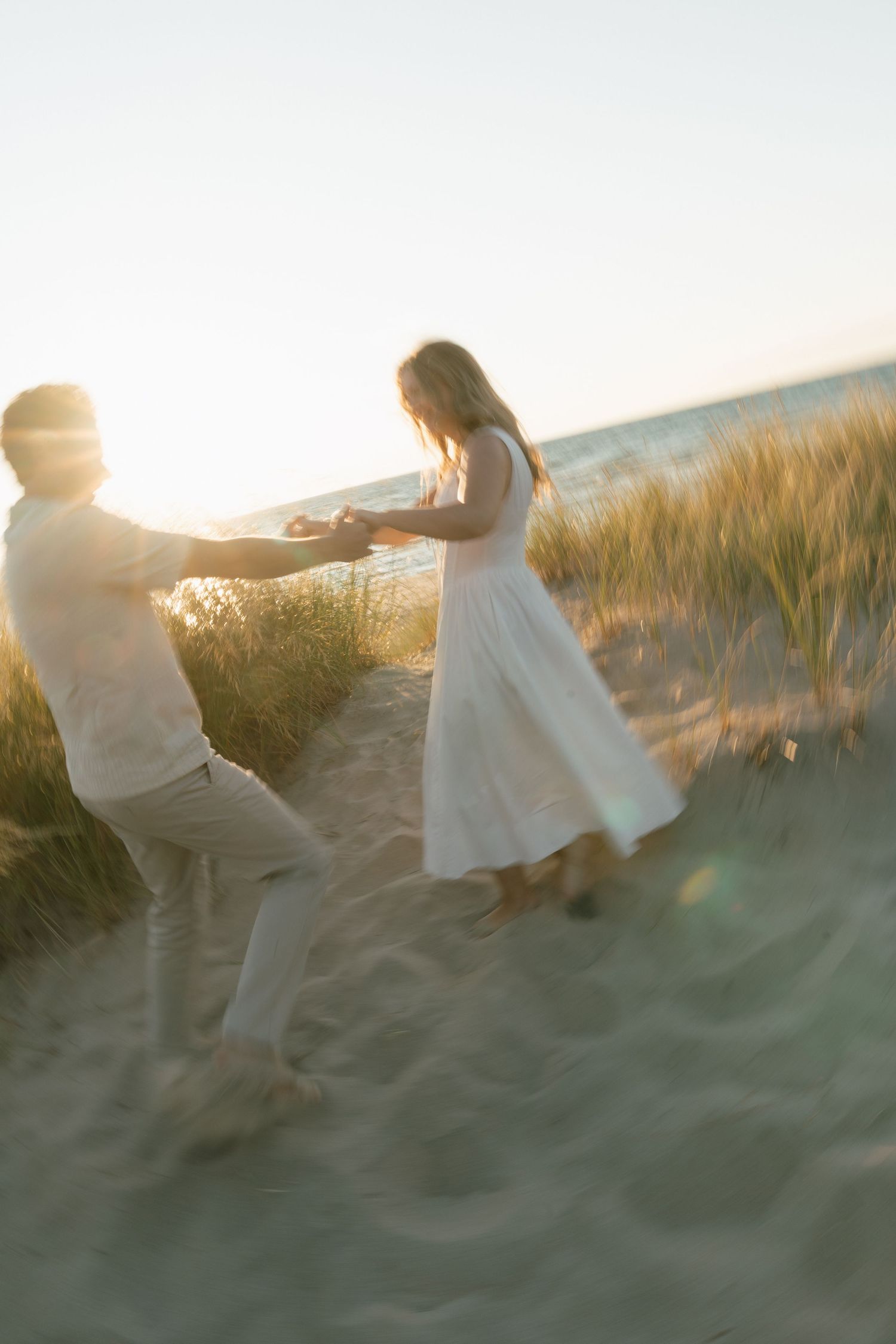 A playful couple holds hands while running through sand dunes at sunset.