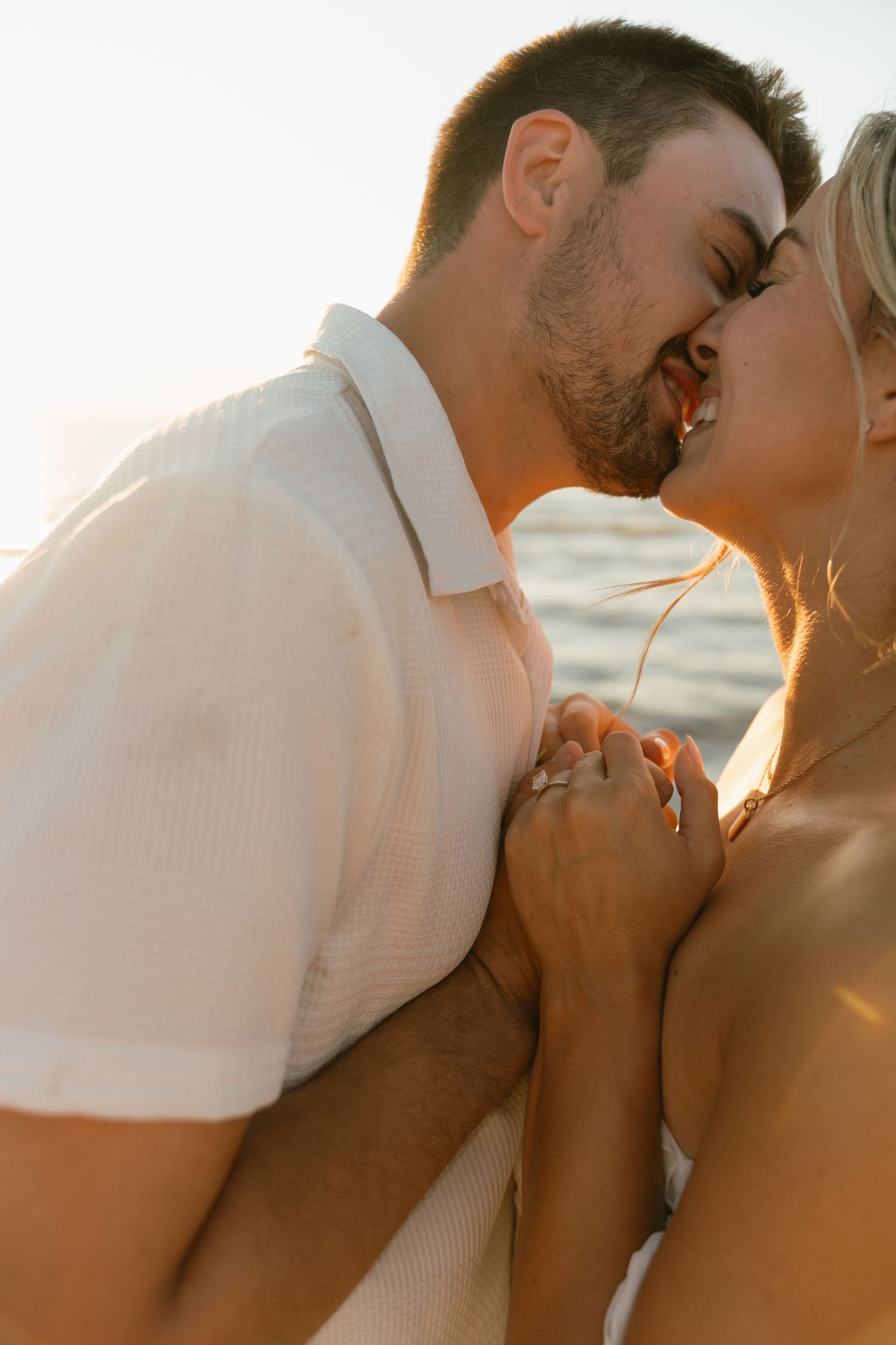 A romantic beach portrait of a couple kissing in golden sunlight.