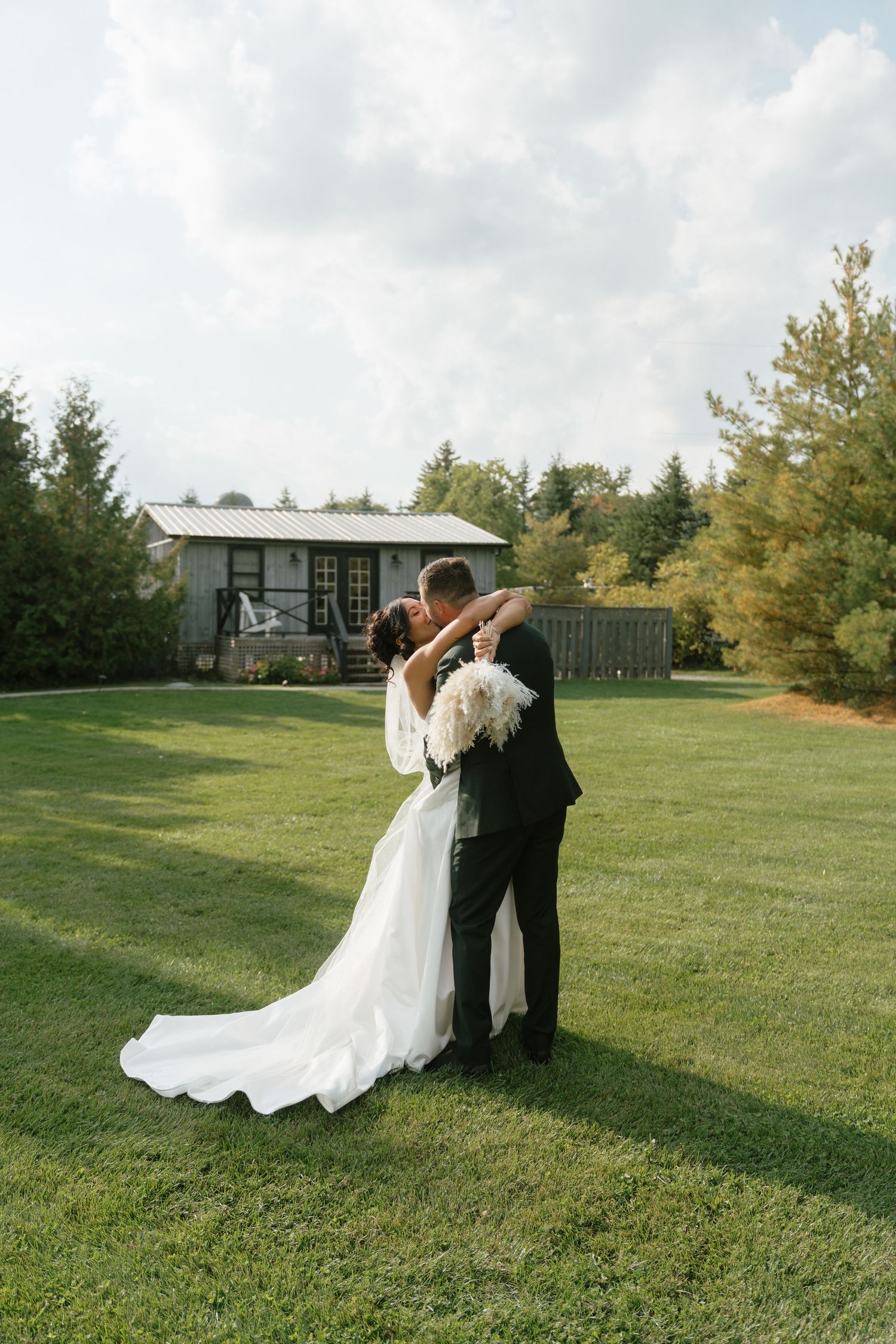Newlyweds embrace on a manicured lawn with a modern venue in the background.