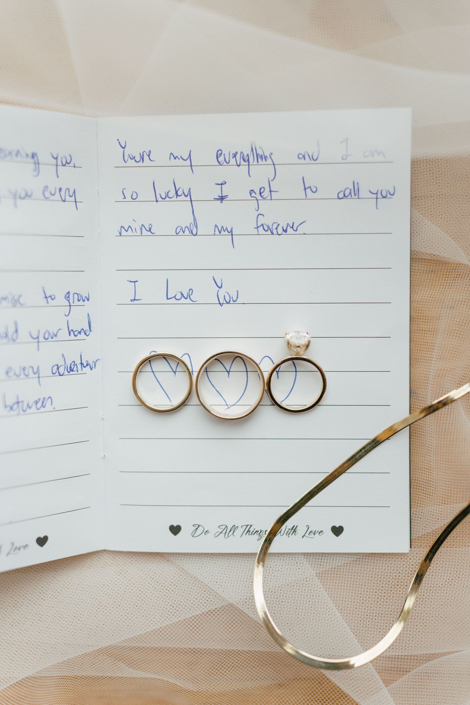 Wedding rings arranged on handwritten love note with delicate veil fabric.