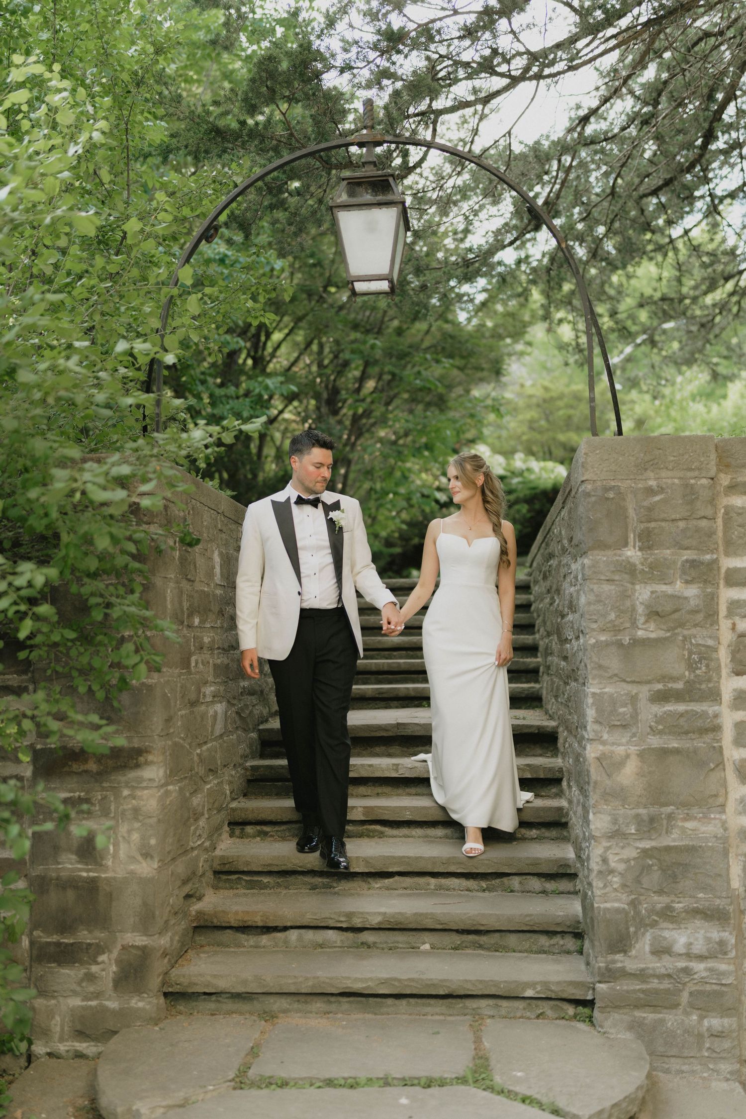 Couple descending stone garden steps under vintage lantern and greenery arch.
