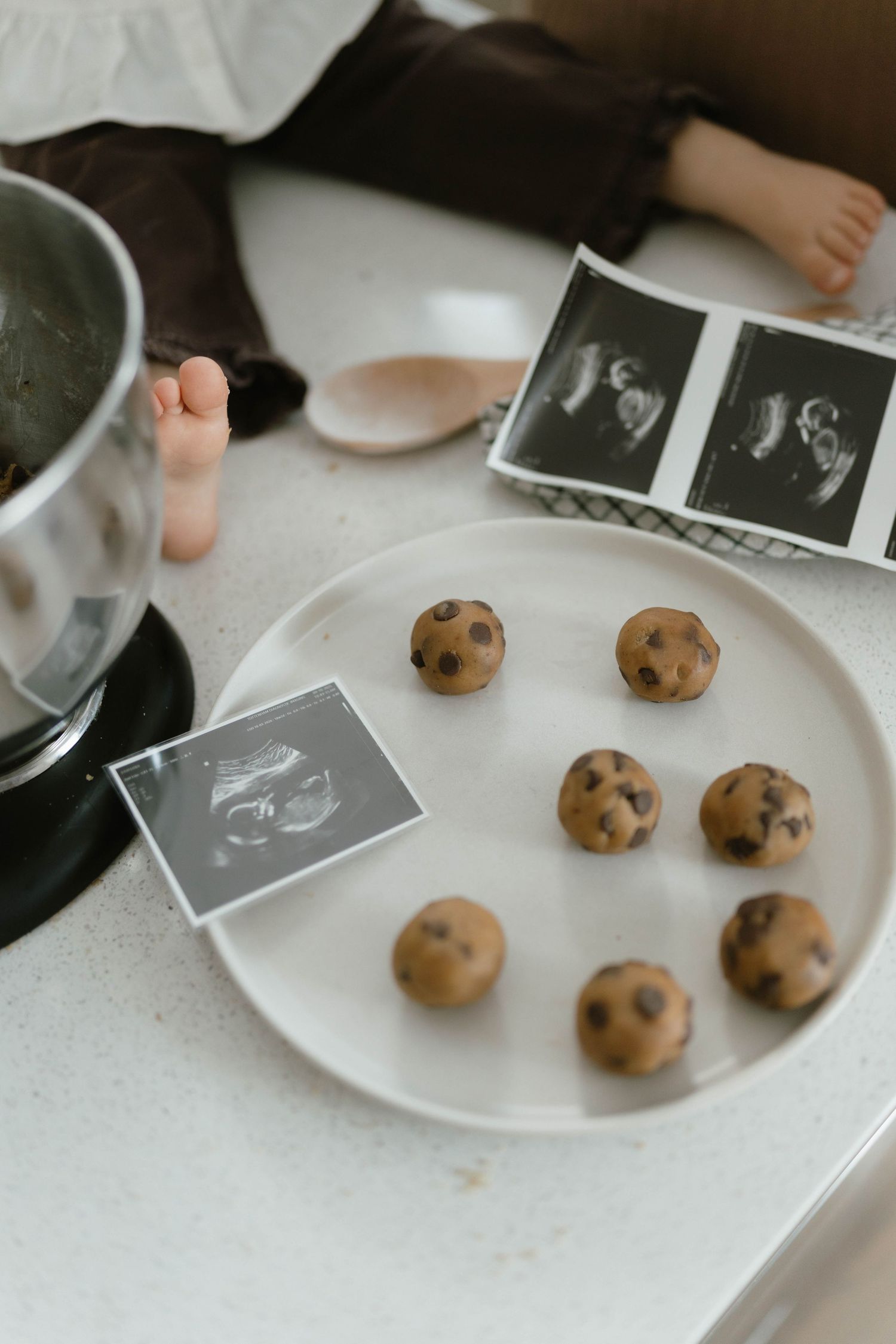 Chocolate chip cookies and ultrasound photos displayed on white plate.