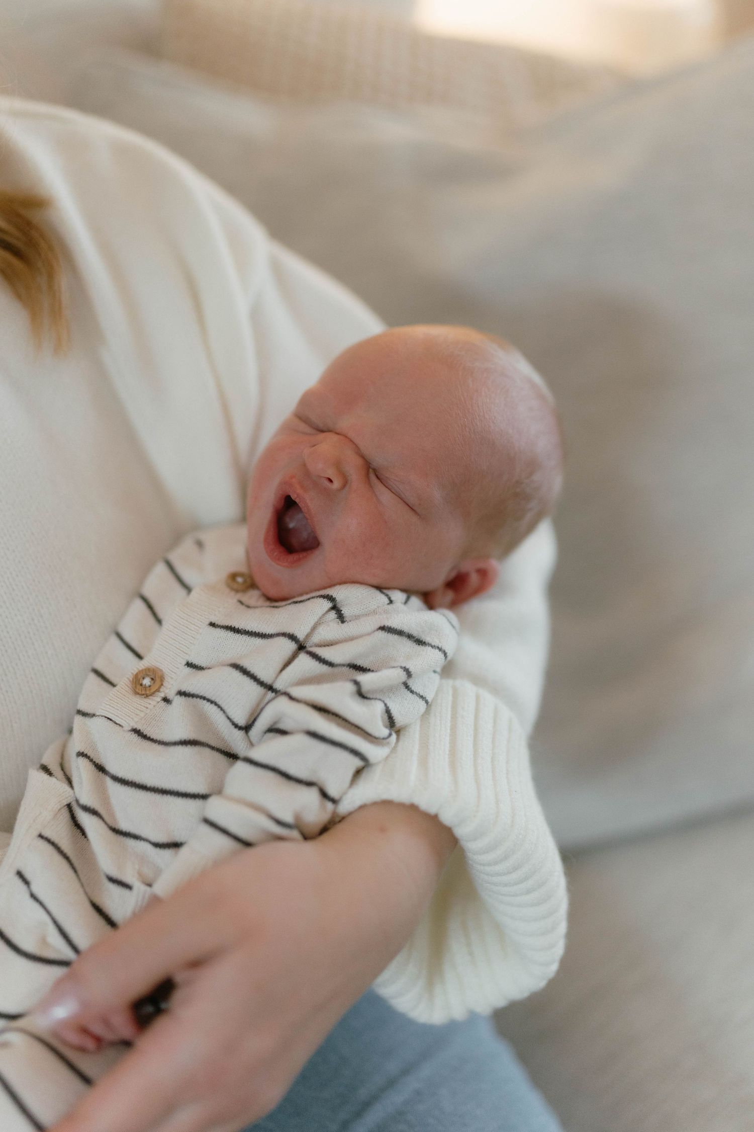Baby in striped outfit yawning and stretching on white bedding.