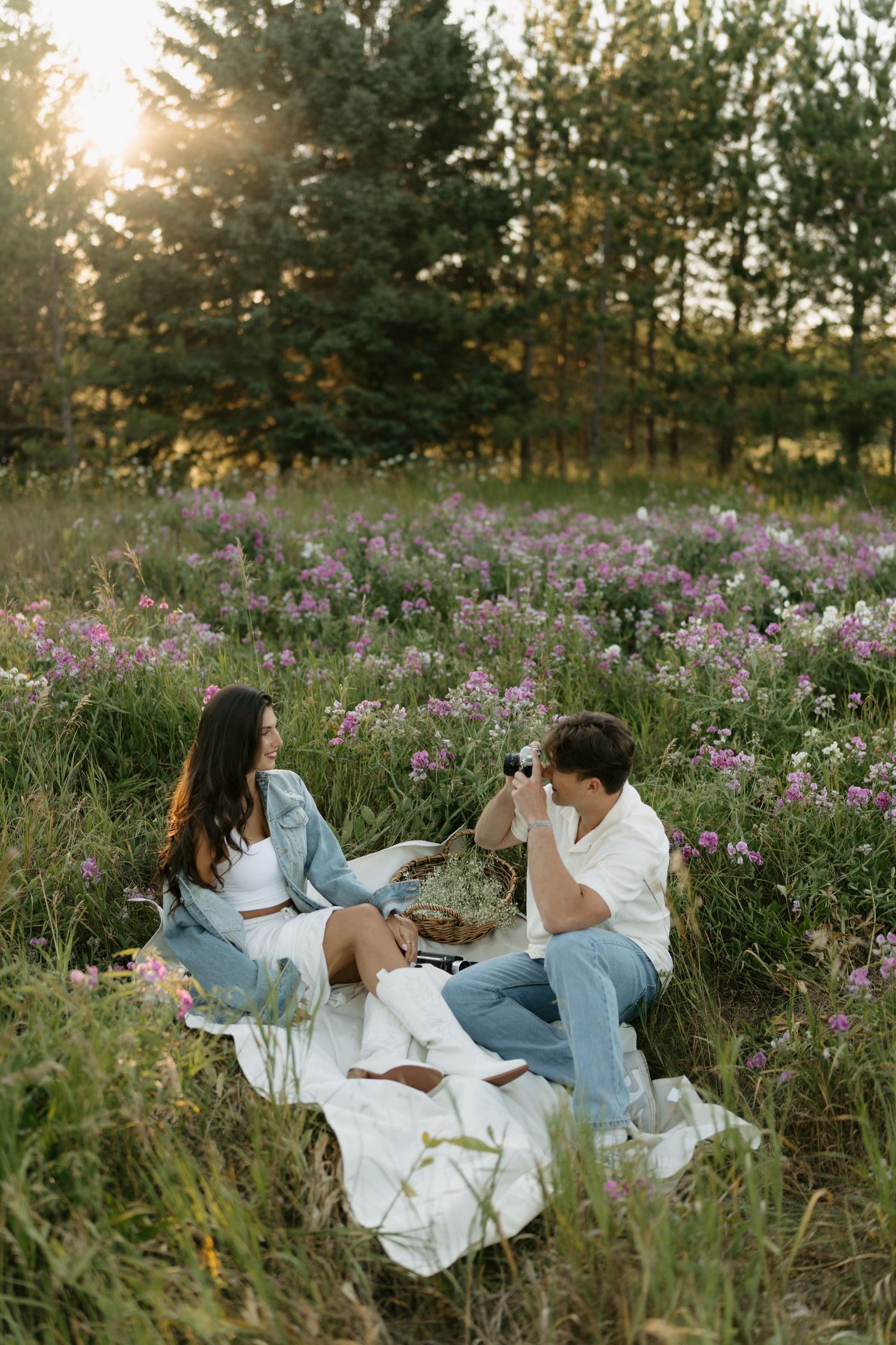 Couple enjoying a romantic picnic in a field of purple wildflowers at sunset.