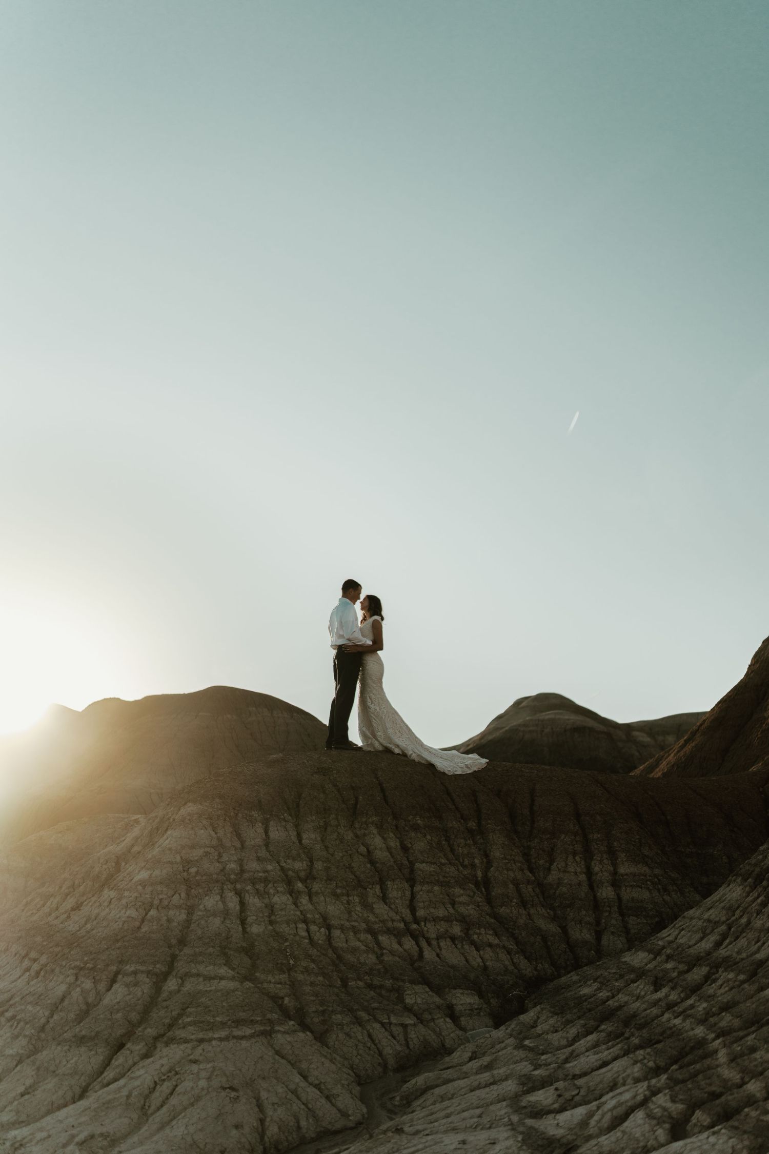 Dramatic silhouette of couple standing on rocky cliff at sunset.