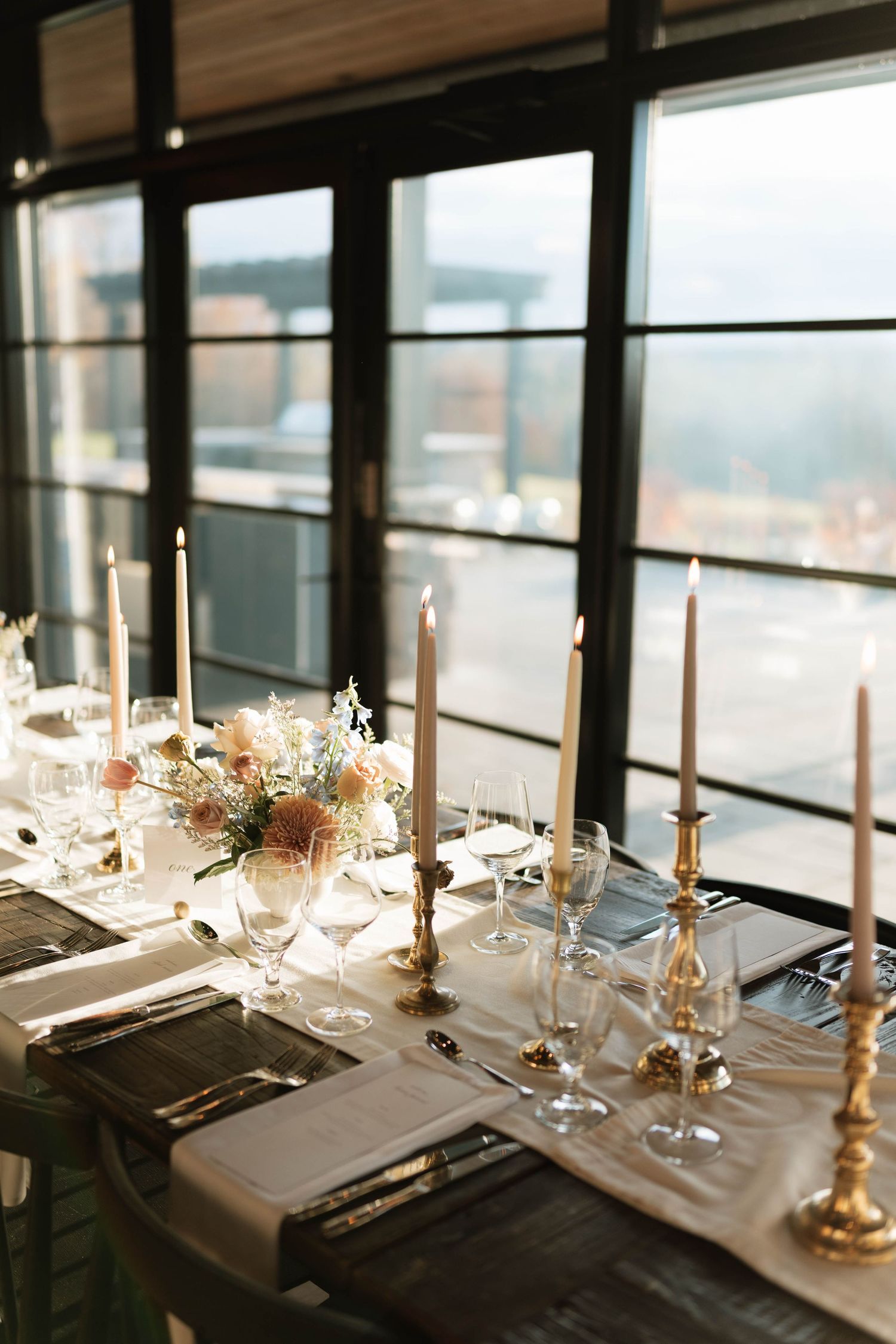 Elegant wedding reception table with tall candles and place settings by window with city view.