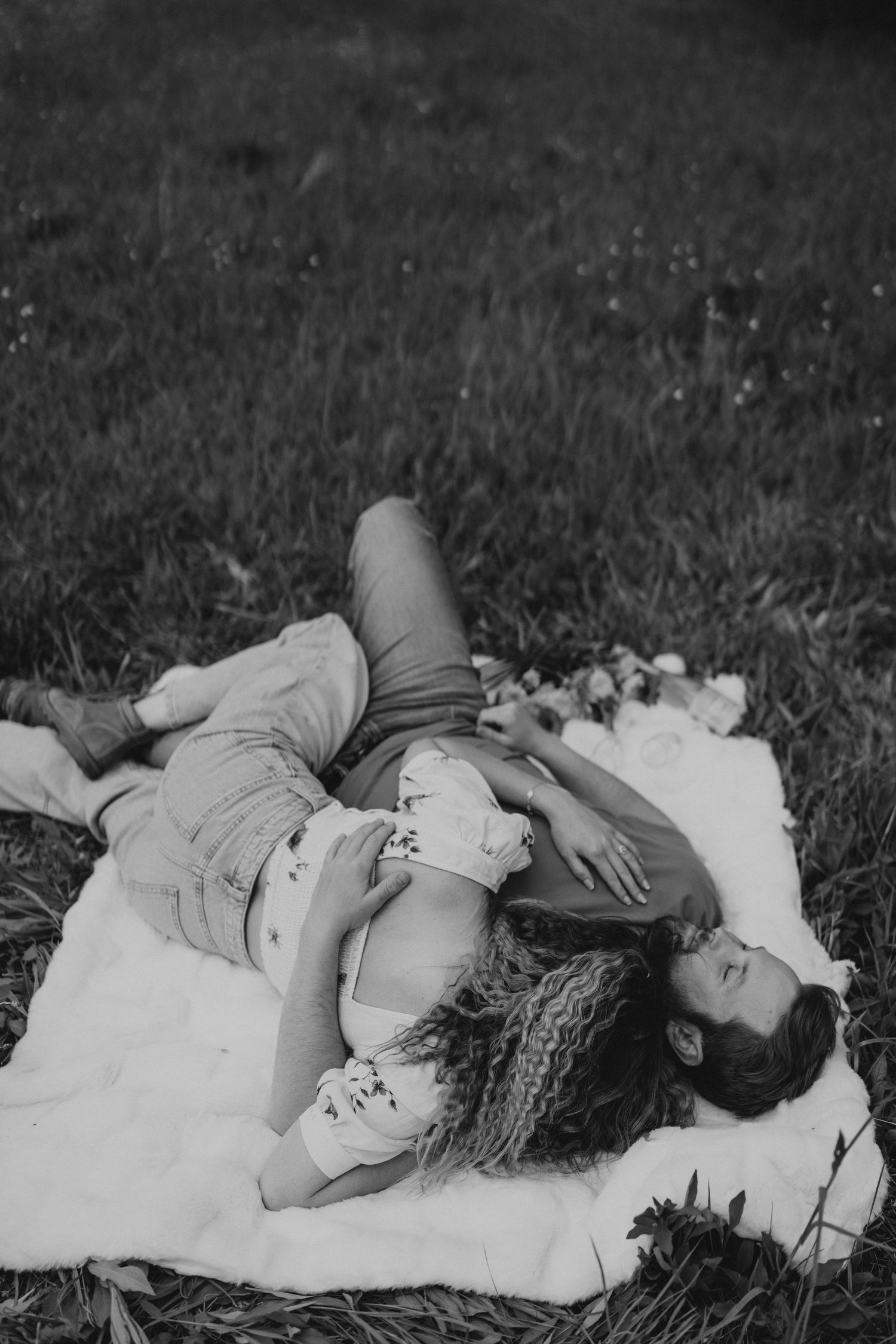 Artistic black and white portrait of someone lying on a blanket in a grassy field.