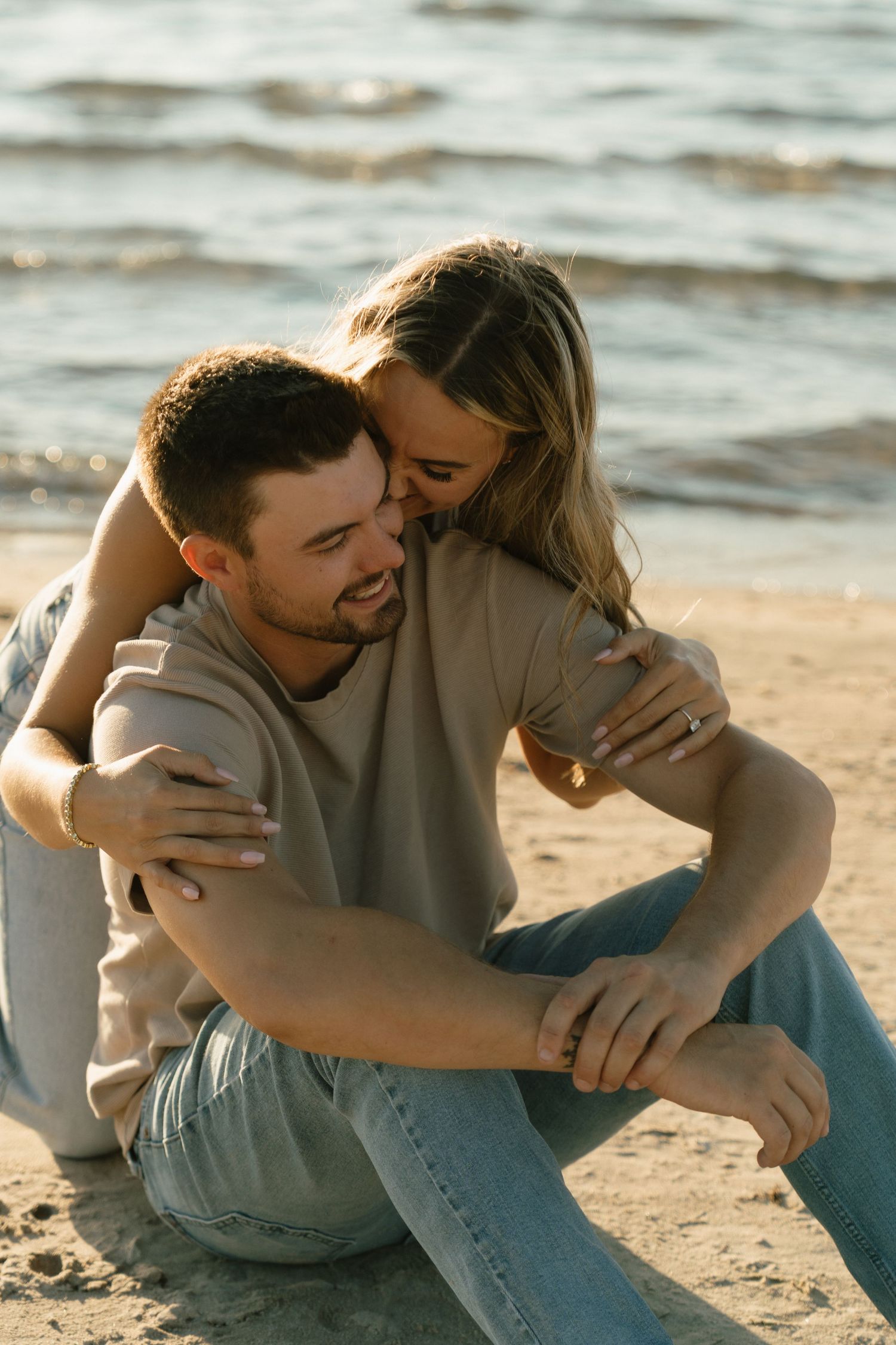 Intimate moment shared between couple sitting on sandy beach at sunset.