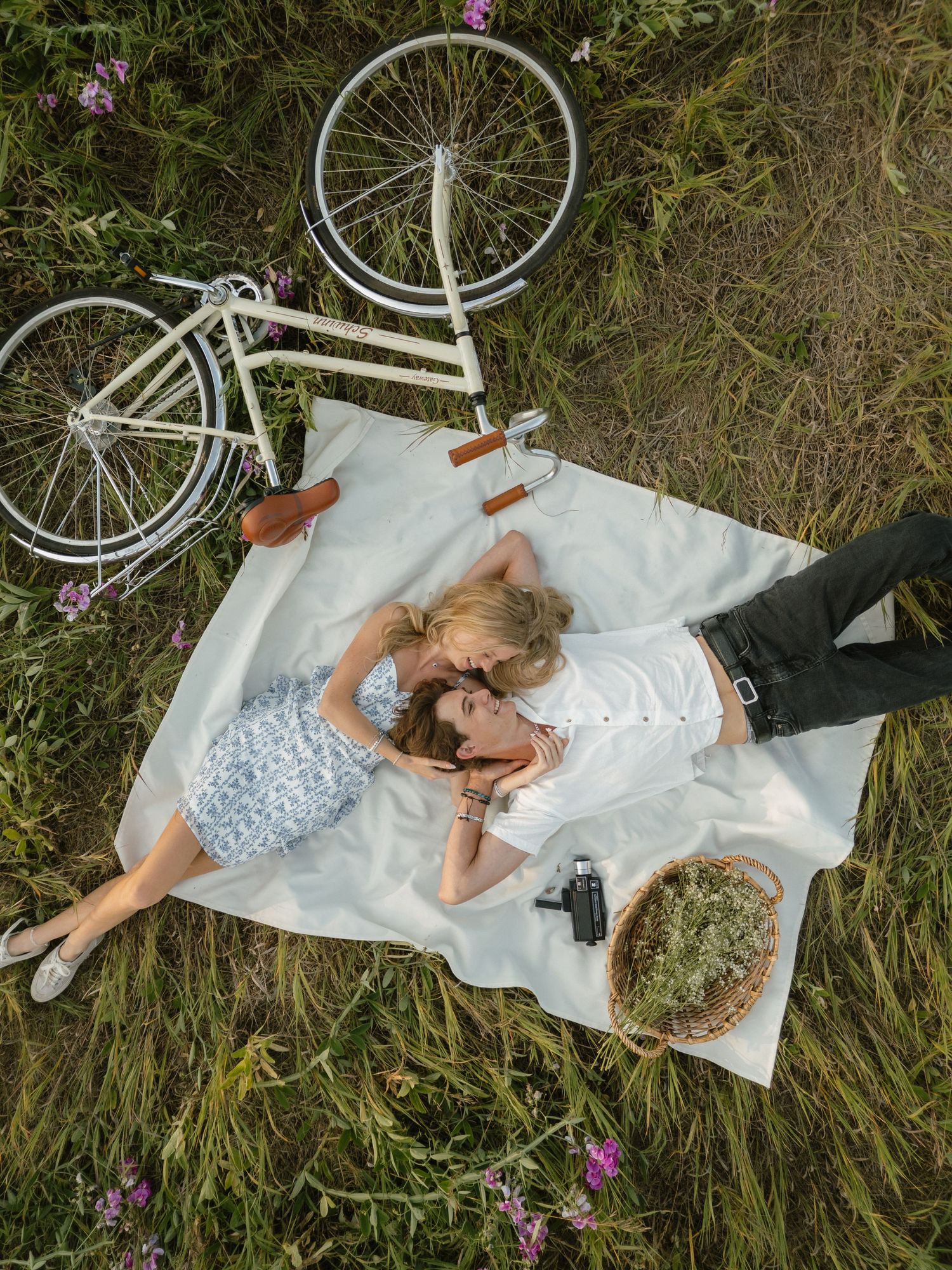 Couple relaxing on a white blanket next to a vintage bicycle in a wildflower meadow.