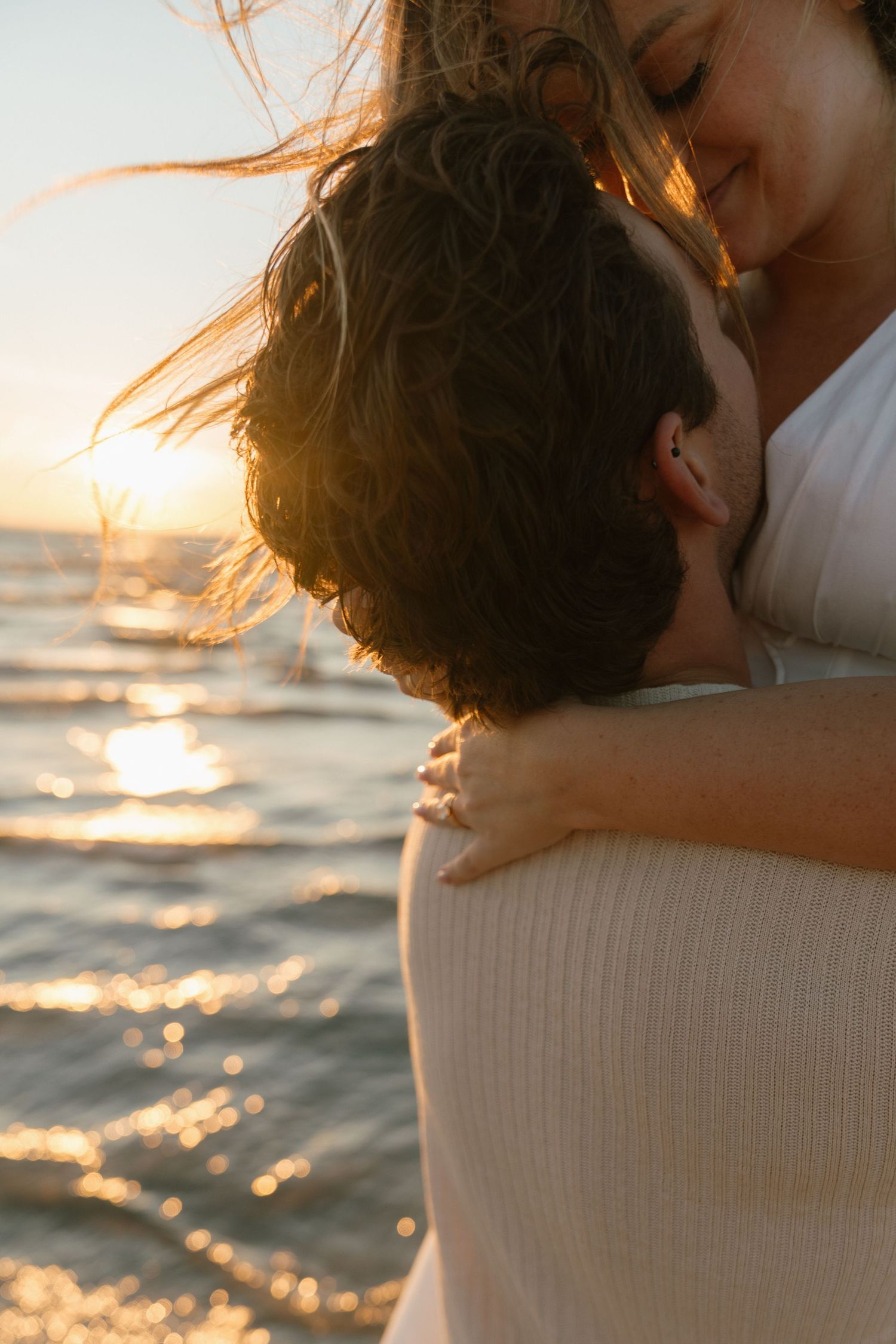 A romantic sunset embrace captured on a beach with golden light reflecting on the water.