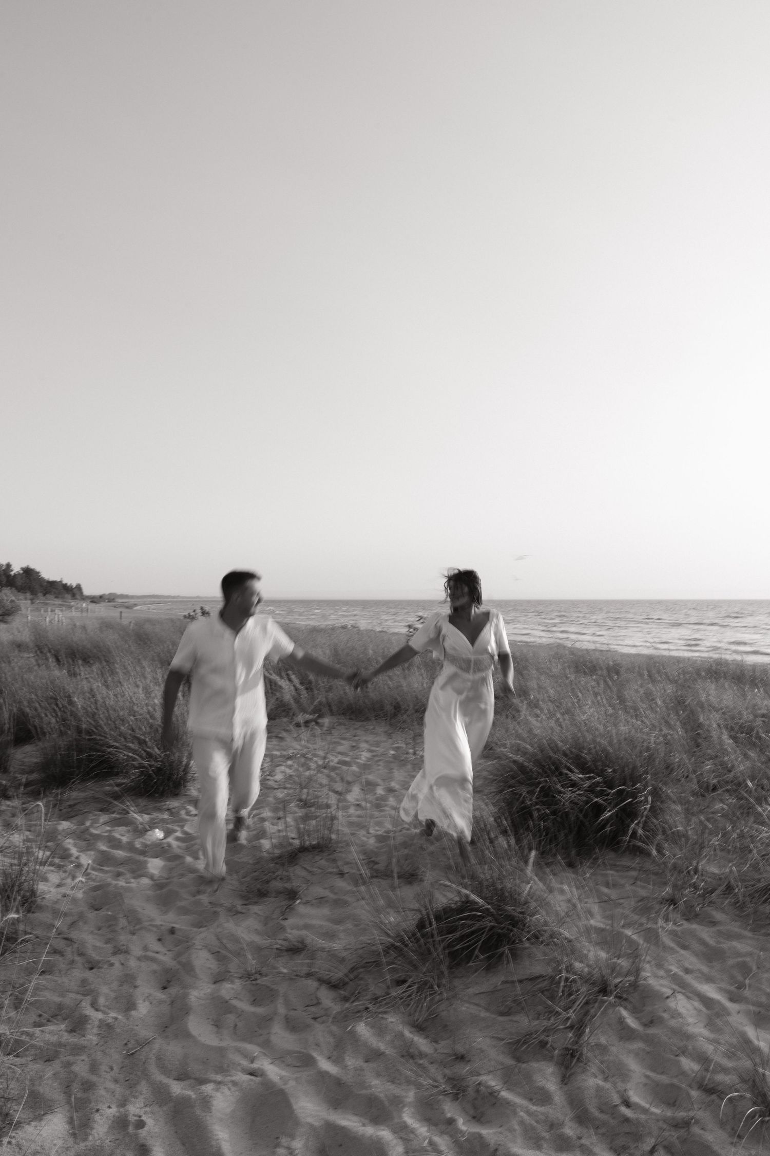 Two figures in white clothing walking along a sandy beach at sunset.