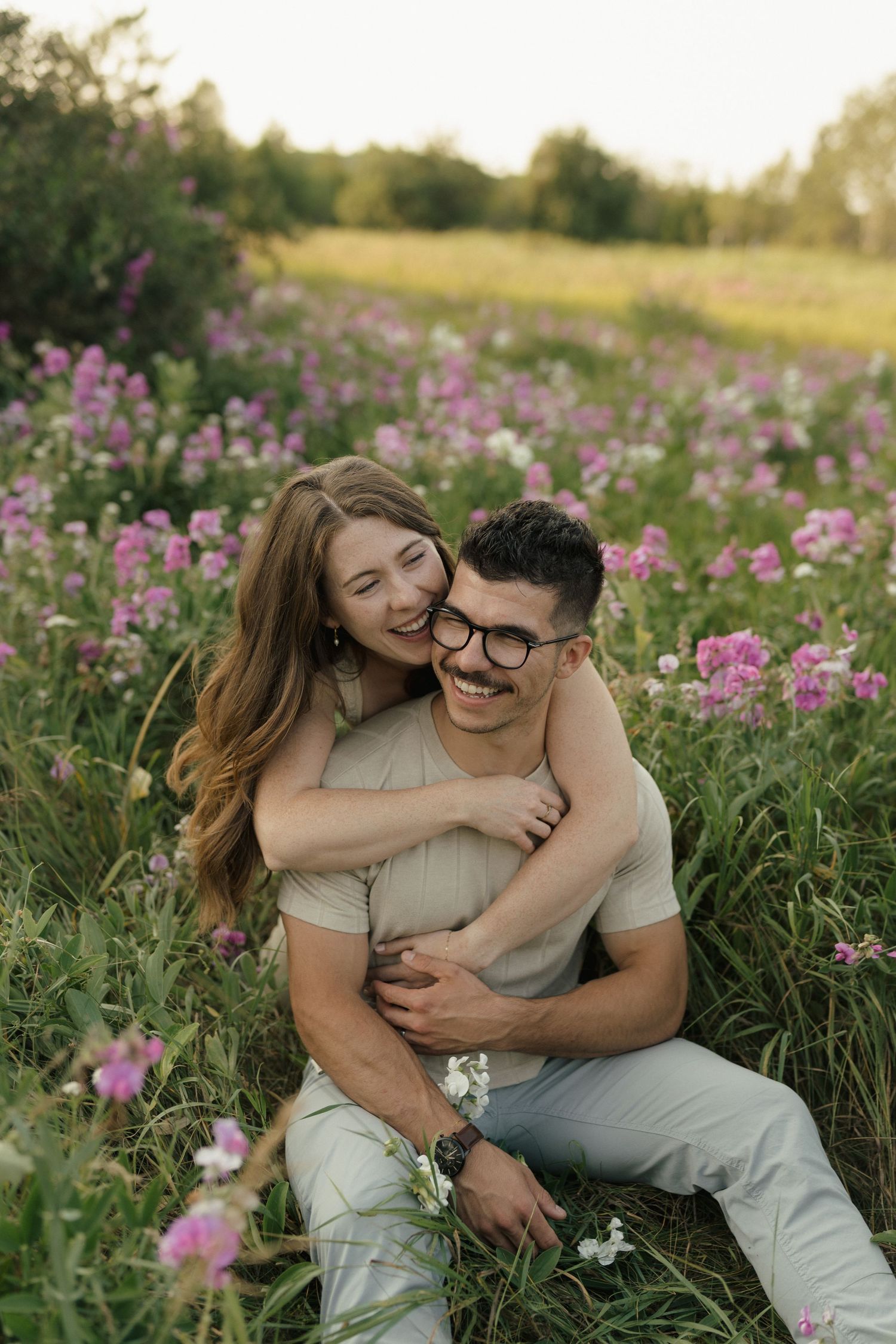 Couple sharing intimate moments in field of pink wildflowers during golden hour.