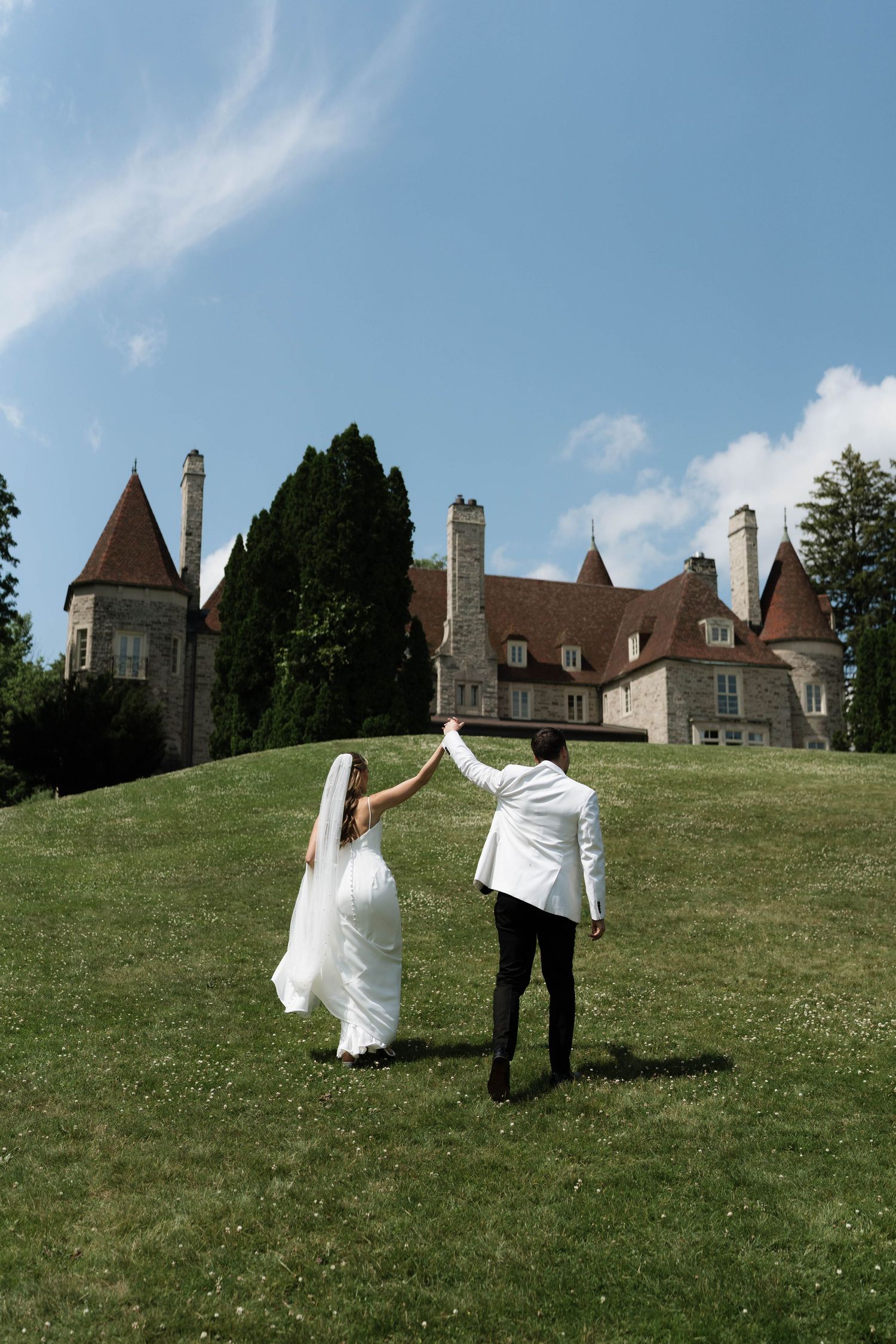 Couple poses on grassy hill with stunning chateau architecture in background.
