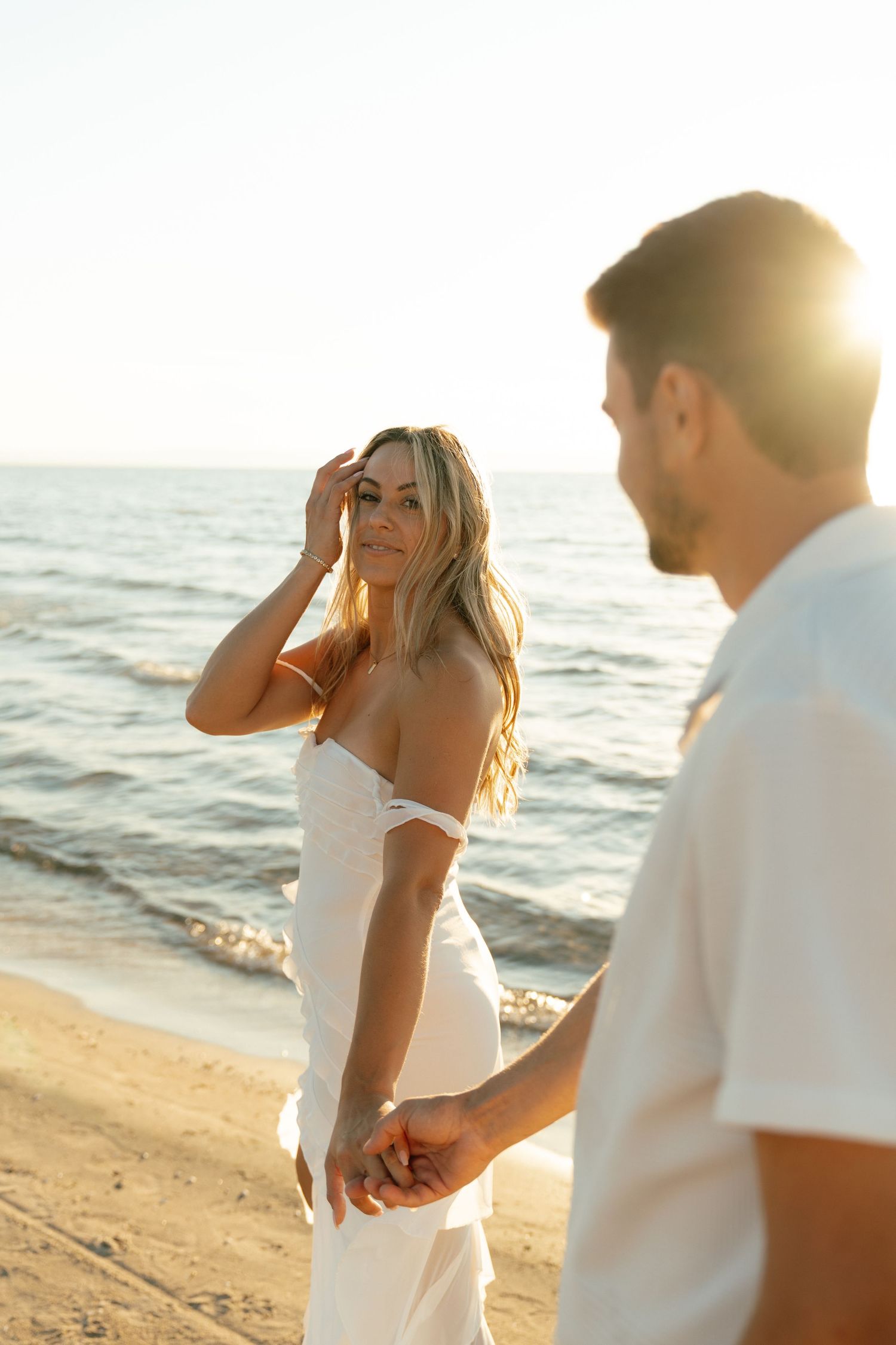 Romantic couple embraces on a sunlit beach during golden hour.