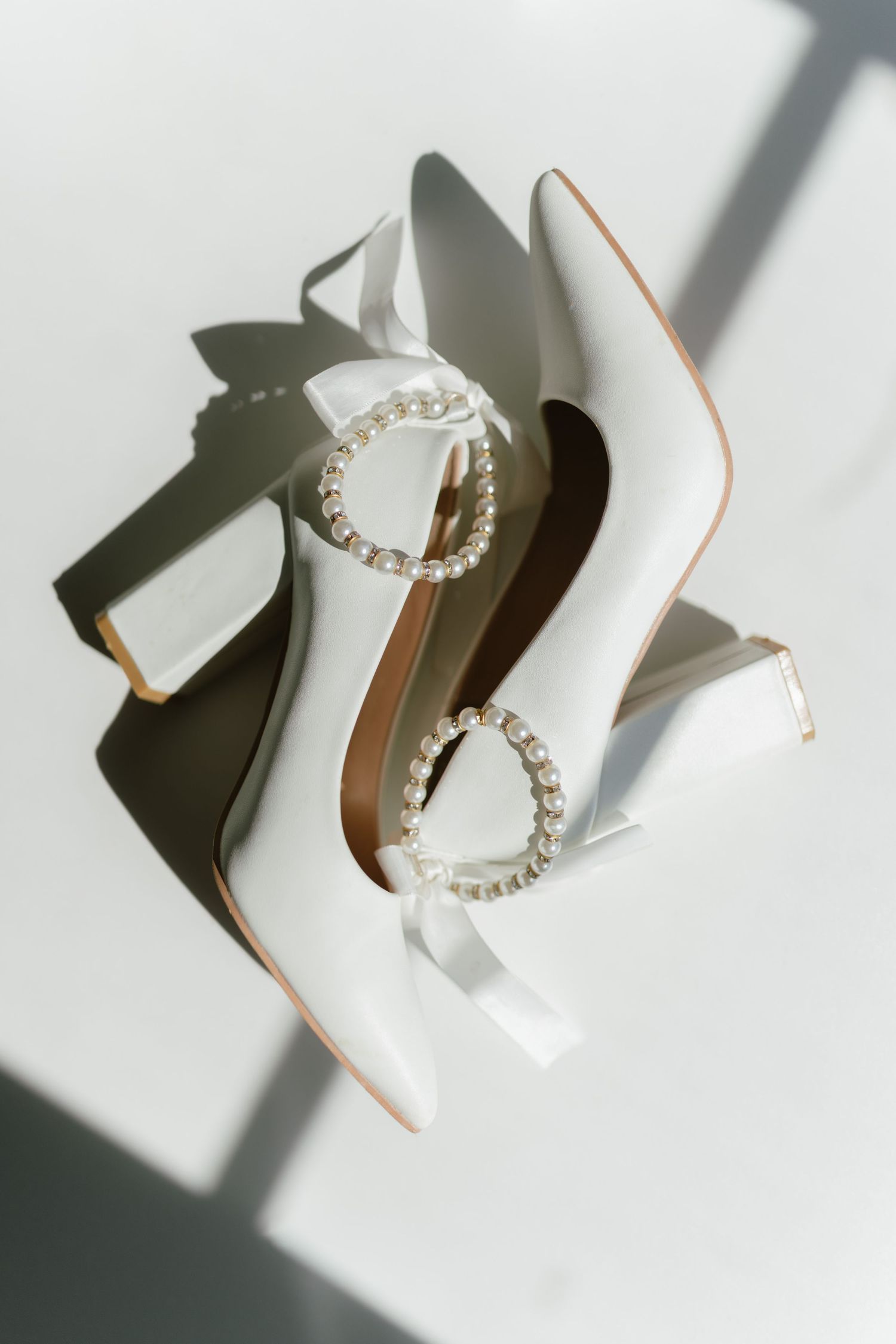 White bridal heels with pearl and crystal embellishments on a white surface with soft natural lighting.