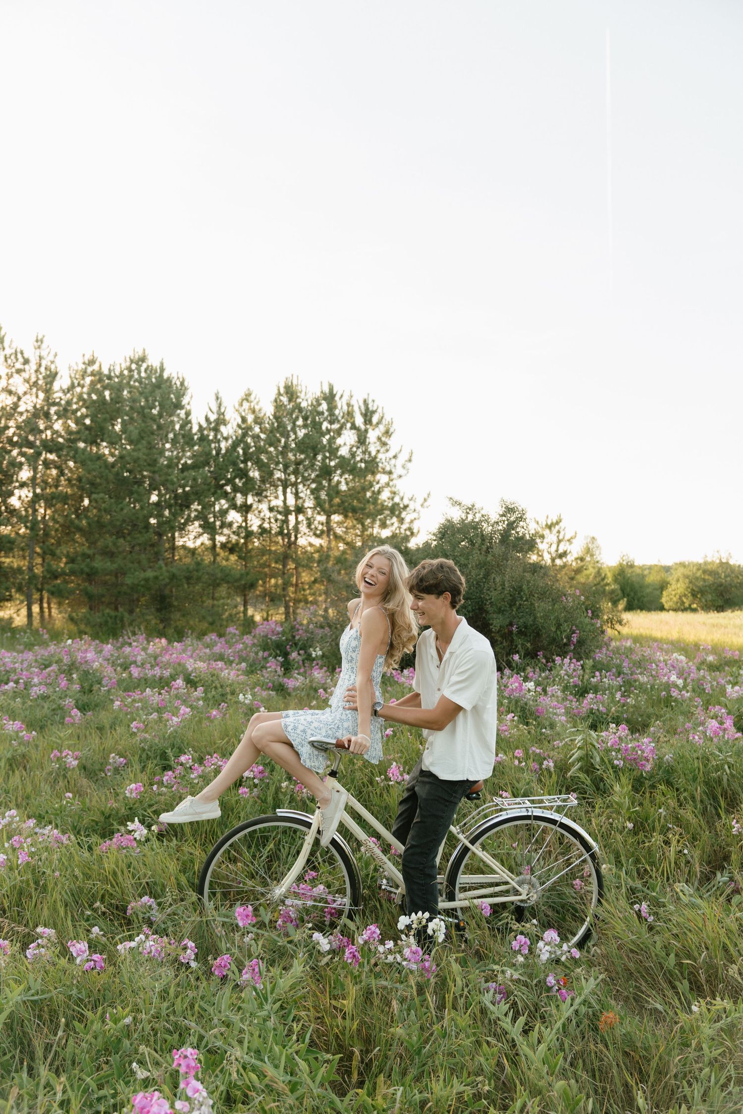 A couple shares tender moments near a white bicycle in a meadow of pink wildflowers.