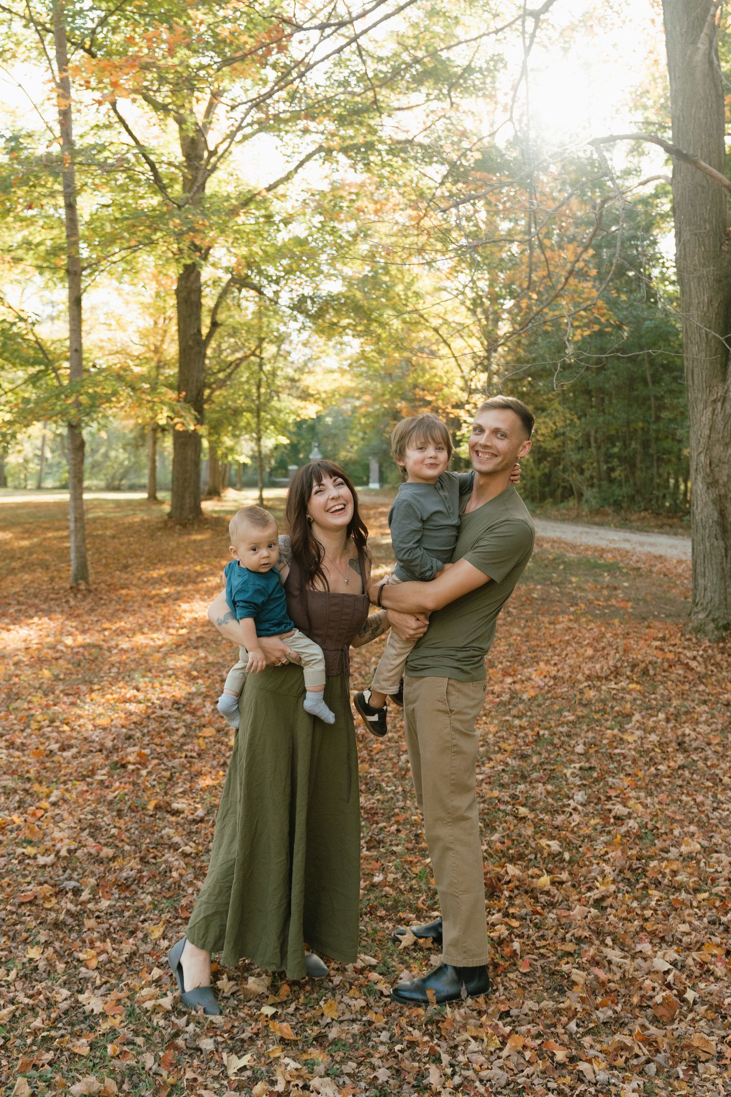 Family of three taking autumn photos among fallen leaves in park.