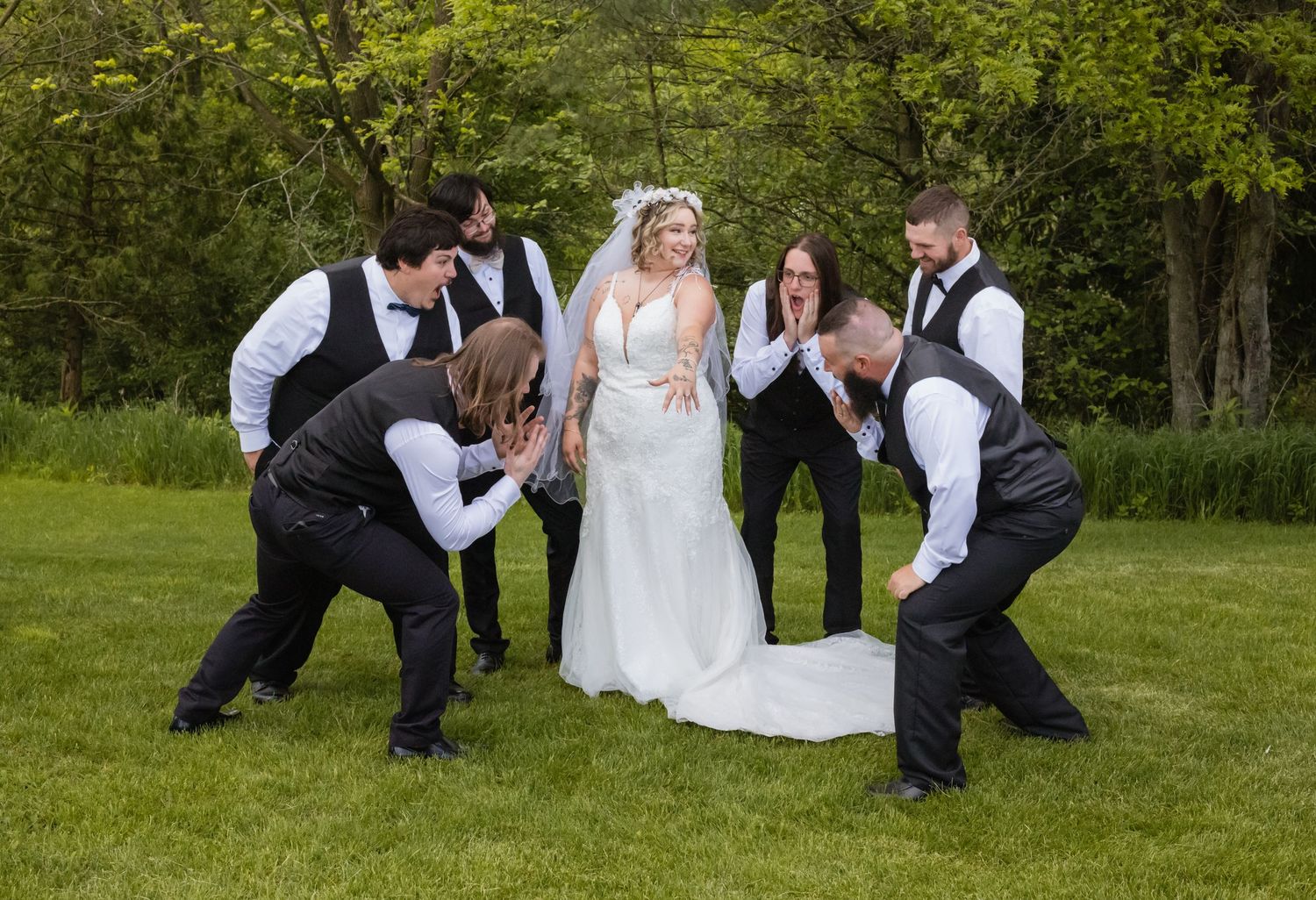Wedding party members playfully pose on the ground during an outdoor photo session.