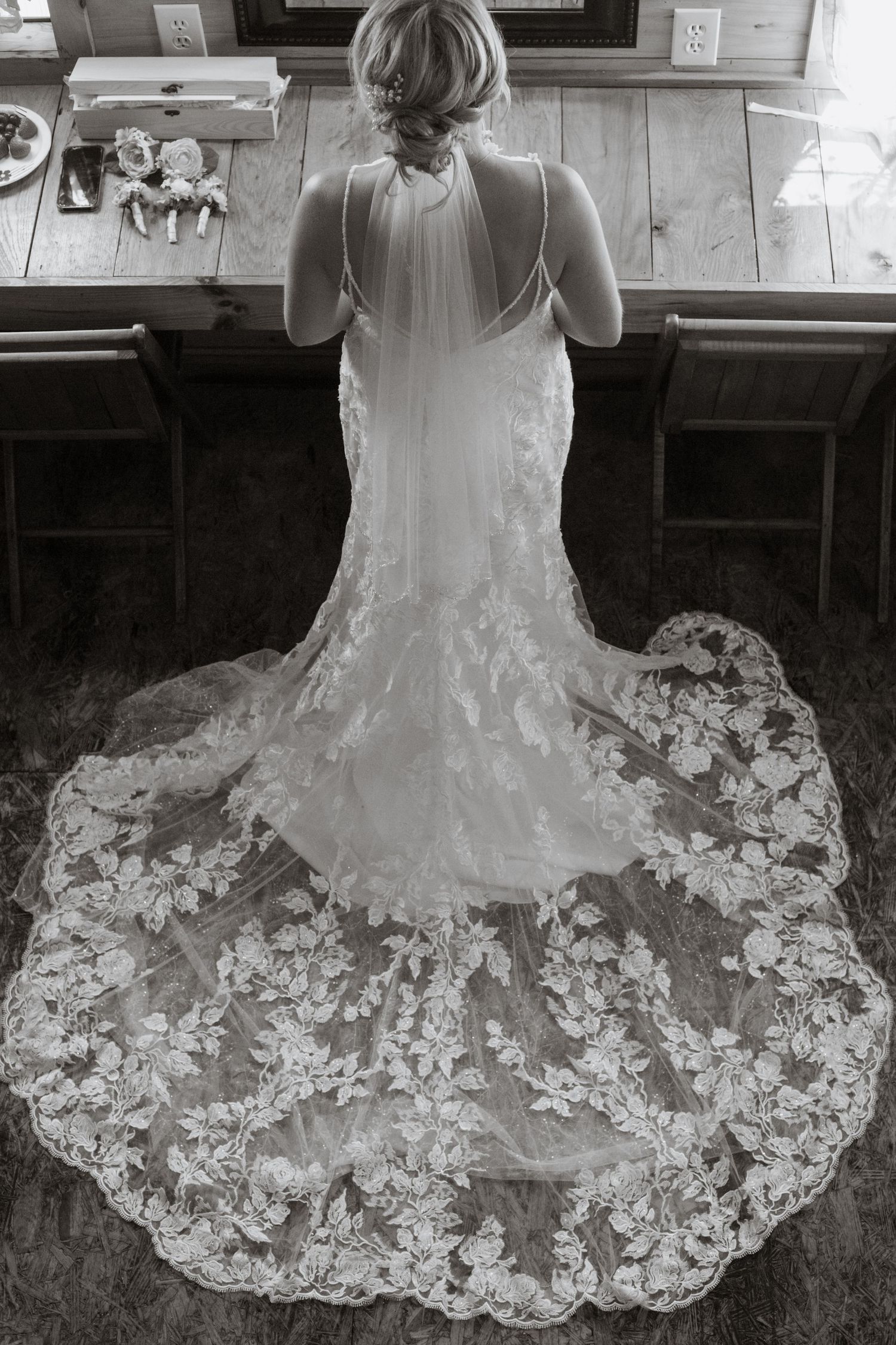 Back view of intricate lace wedding dress with long train on wooden floor.